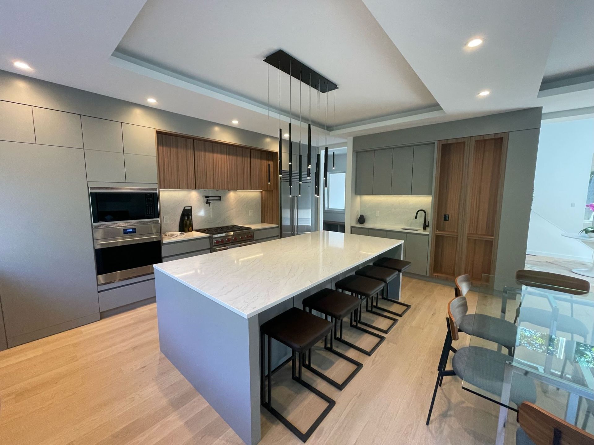 Modern kitchen with white island, black stools, wood cabinets, and stainless steel appliances