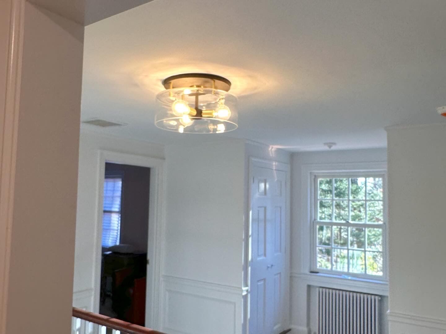Bright hallway with white walls, ceiling light, and a window above a radiator.