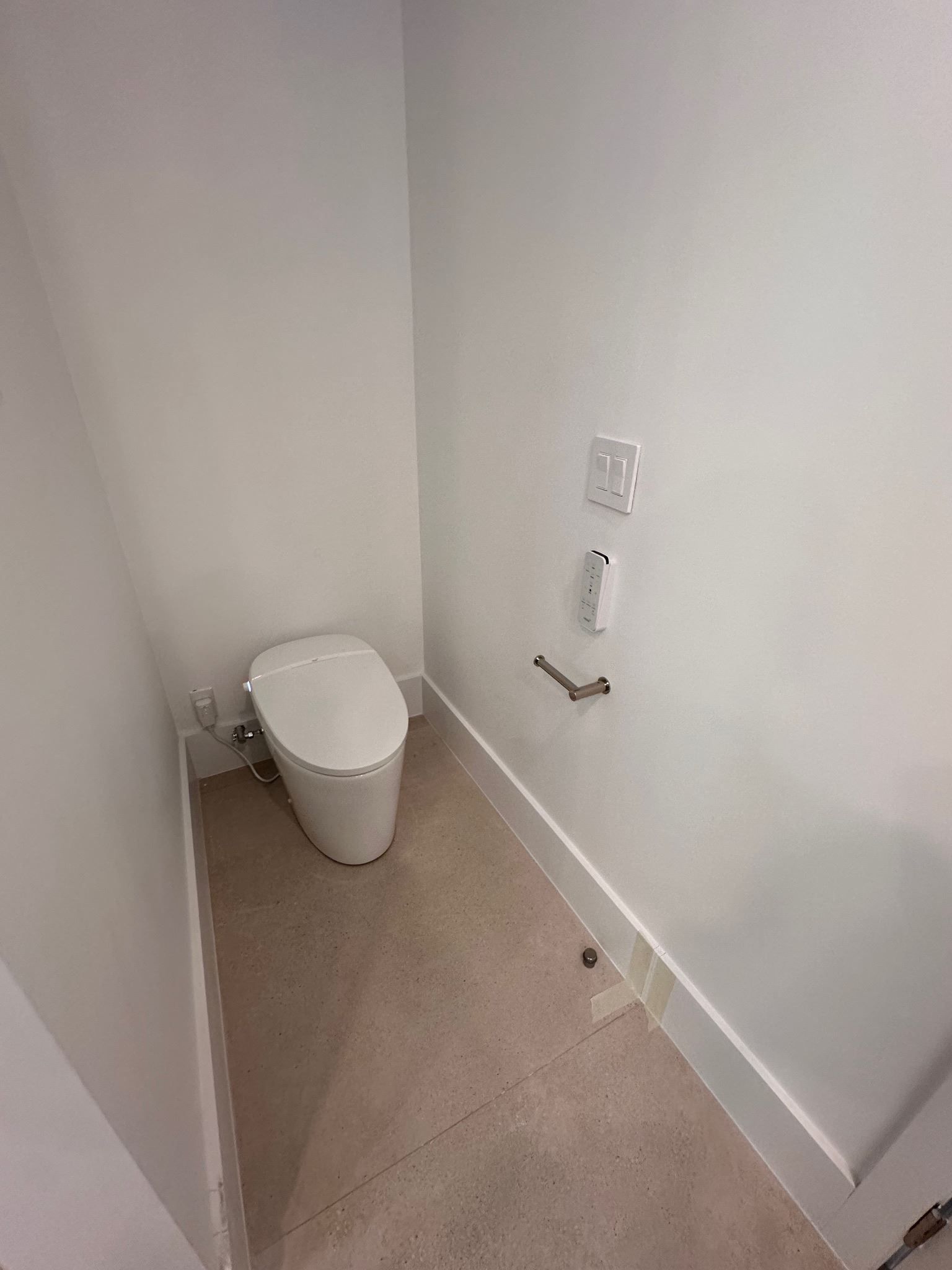 Small white bathroom with a toilet in the corner and a wall-mounted control panel.