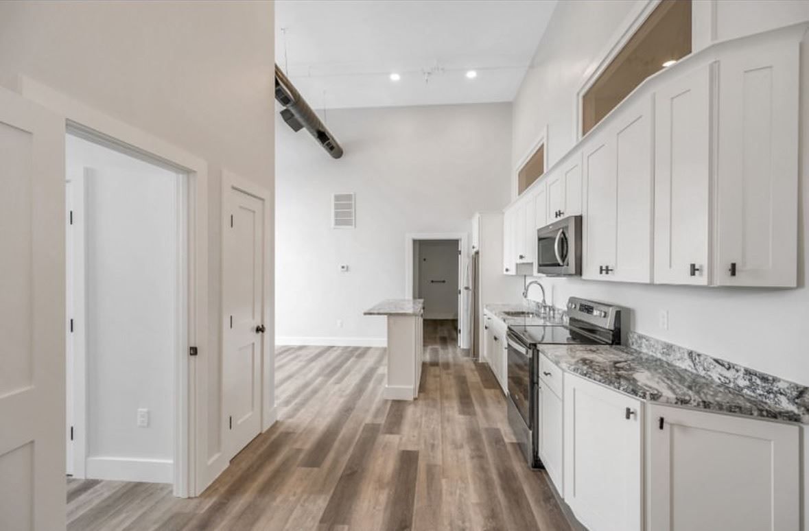 Bright modern kitchen with white cabinets, stainless appliances, and wood-look flooring