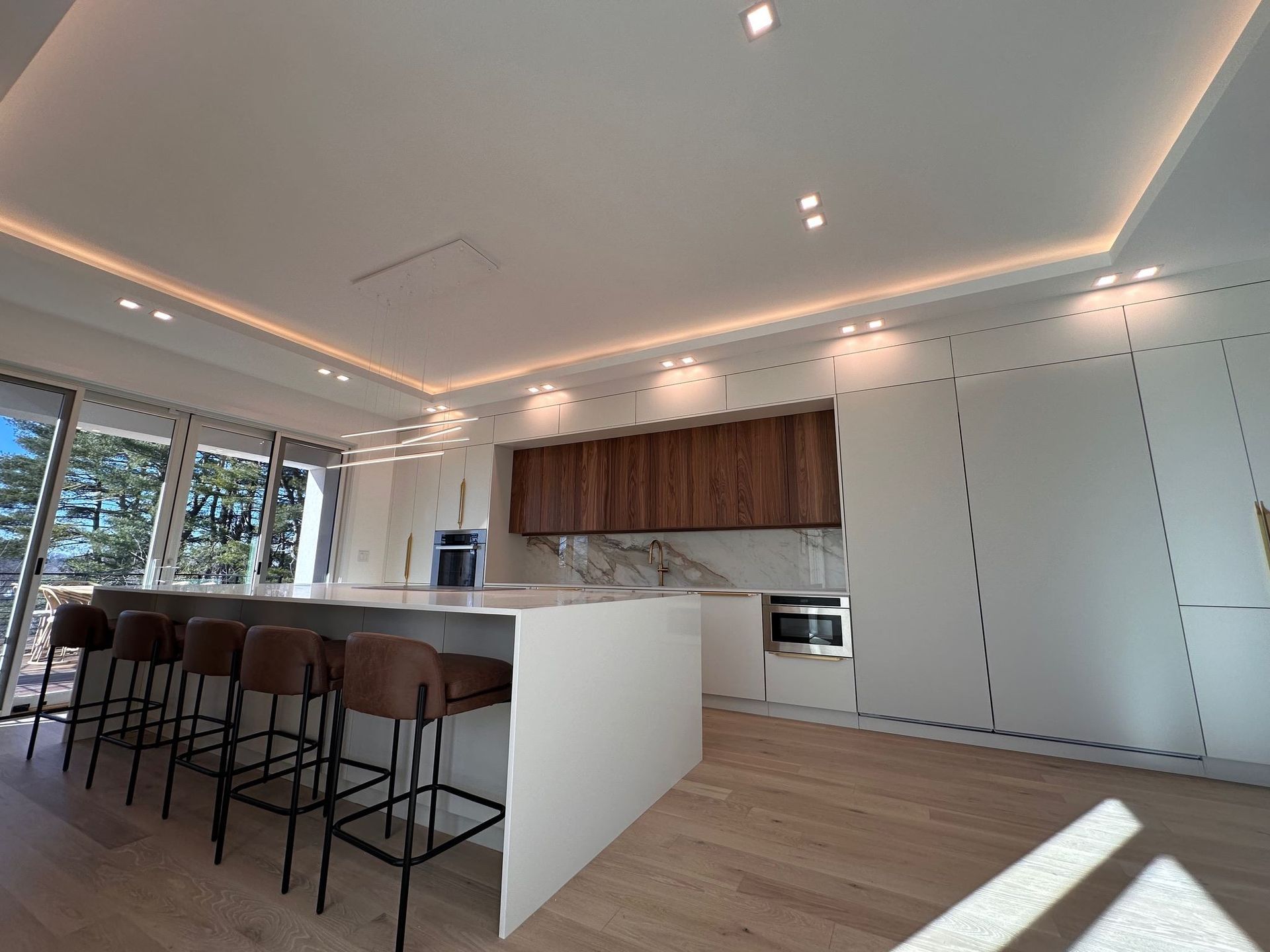 Modern kitchen with white island, bar stools, wood cabinets, and large windows.