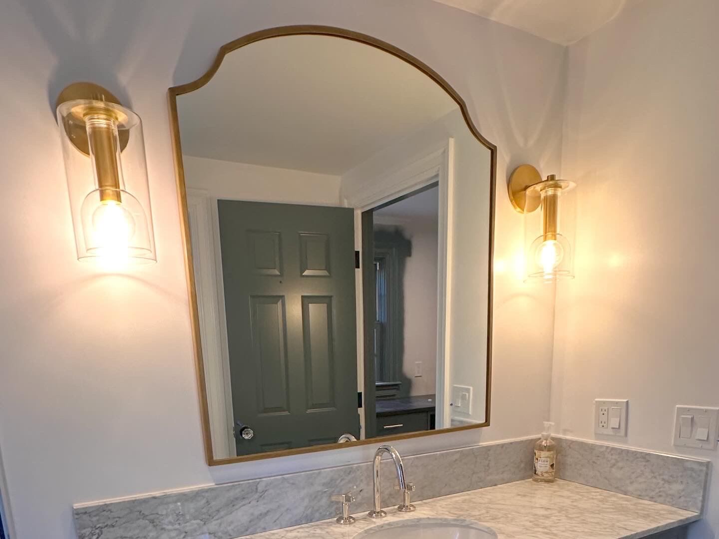 Bathroom vanity with gold-framed mirror, wall sconces, and gray countertop sink