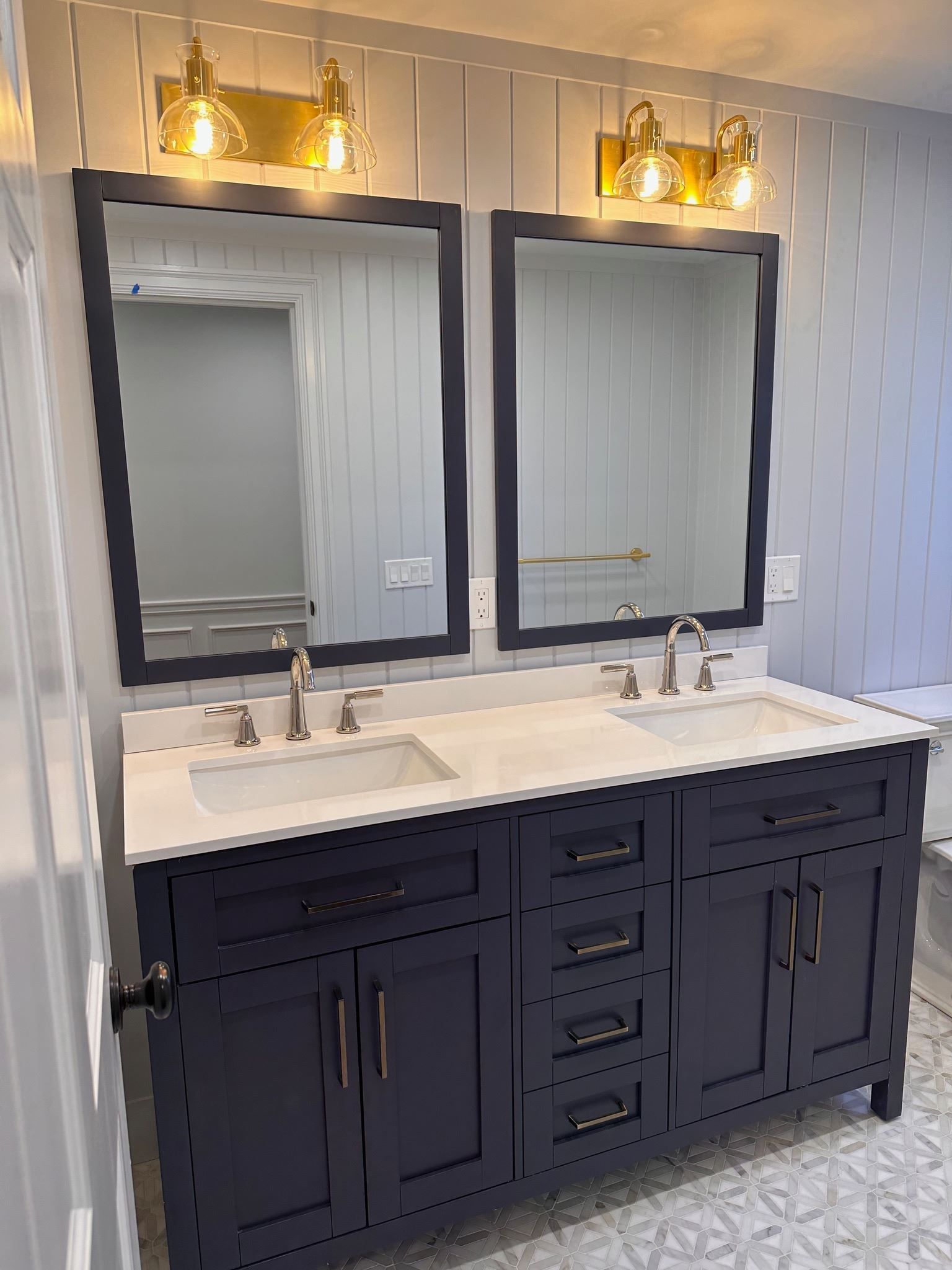 Modern double bathroom vanity with black cabinets, white countertop, and two framed mirrors under warm wall lights
