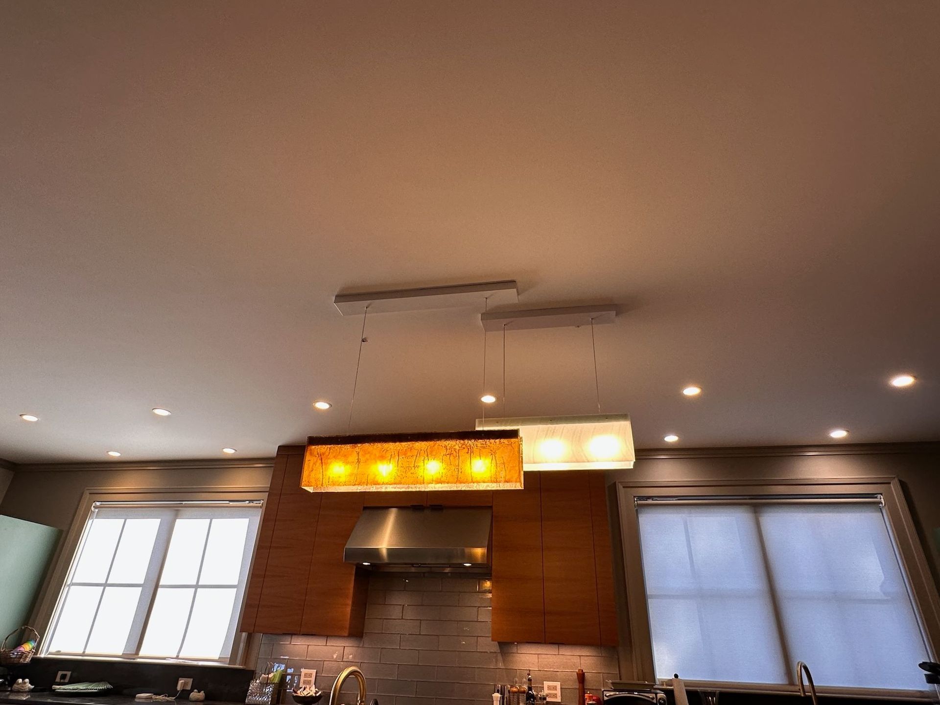 Modern kitchen interior with recessed lights, wood cabinets, and two windows under a glowing pendant fixture