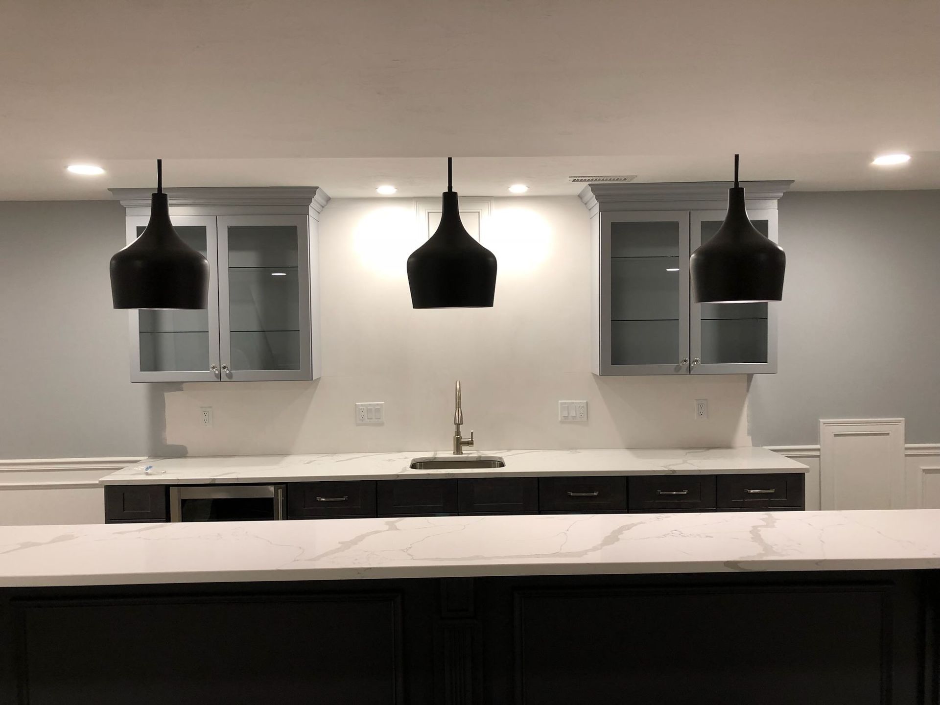 Modern kitchen with white countertops, dark pendant lights, and gray cabinets against a light gray wall
