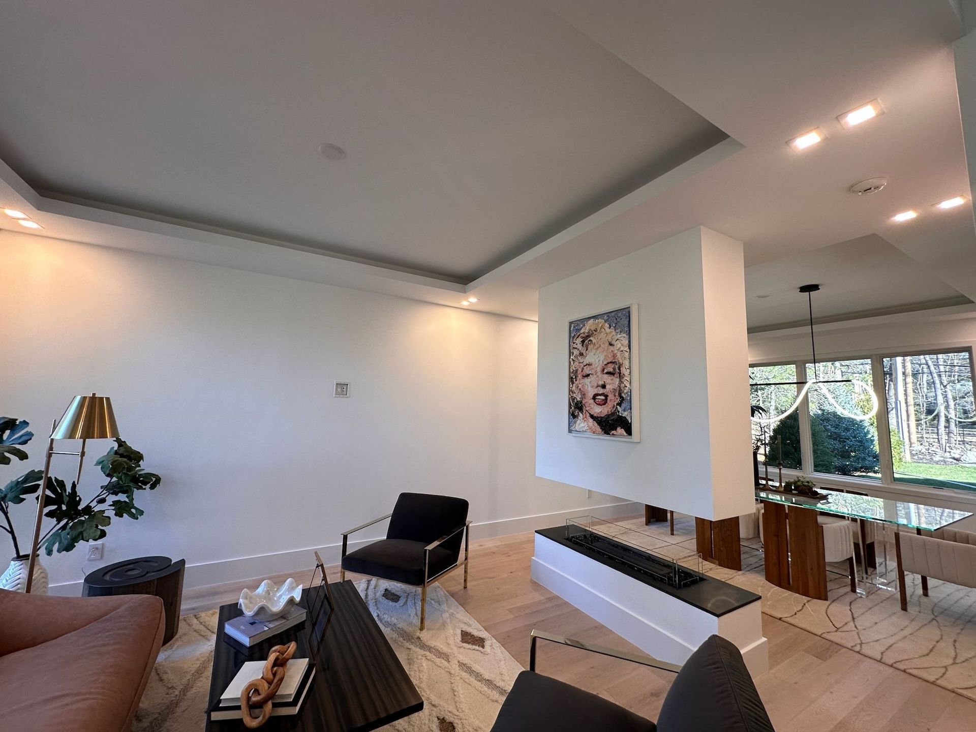 Modern living room with white walls, black chairs, tan sofa, and large windows overlooking trees