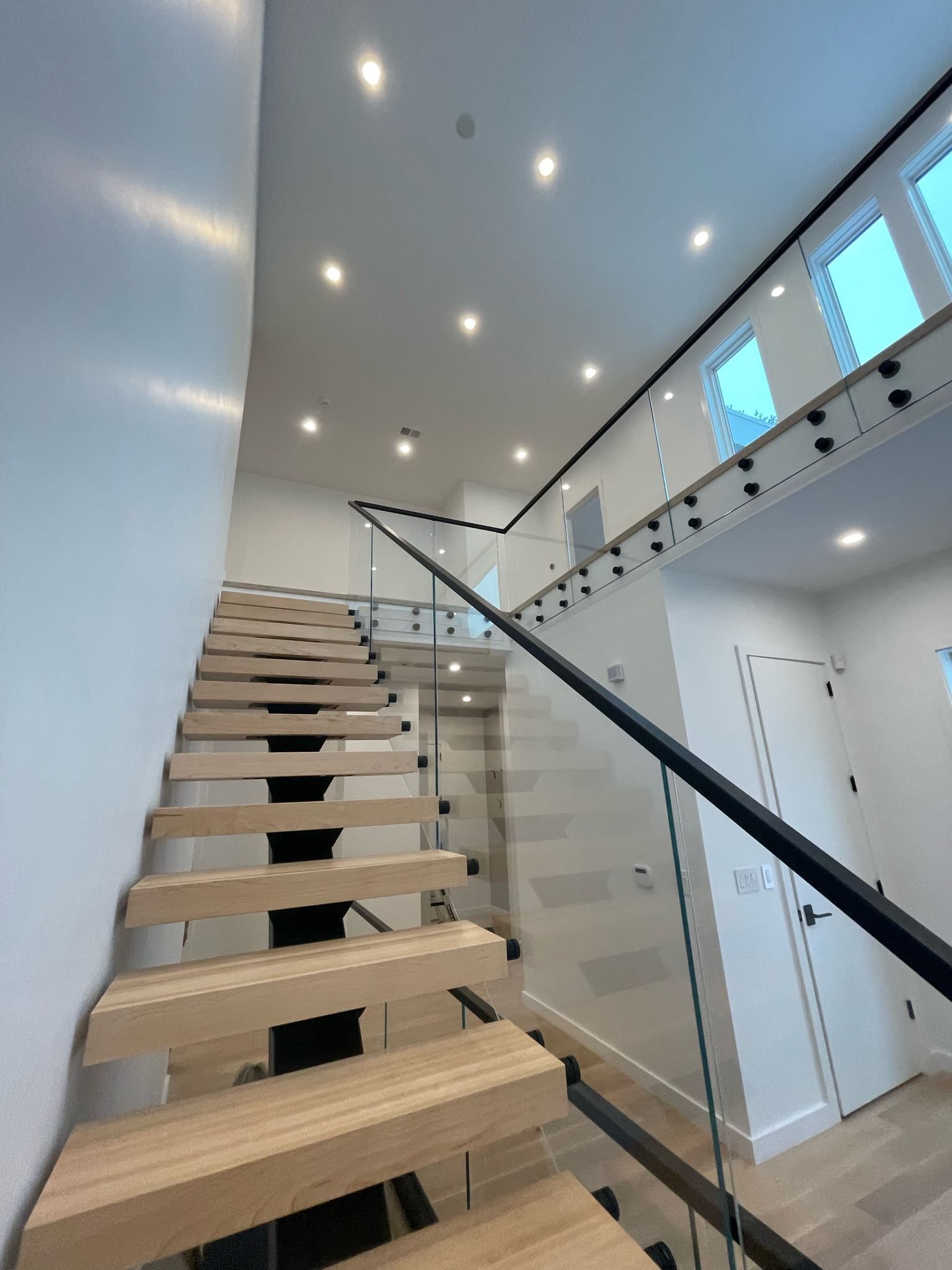 Modern indoor staircase with wooden steps, glass railing, and recessed ceiling lights
