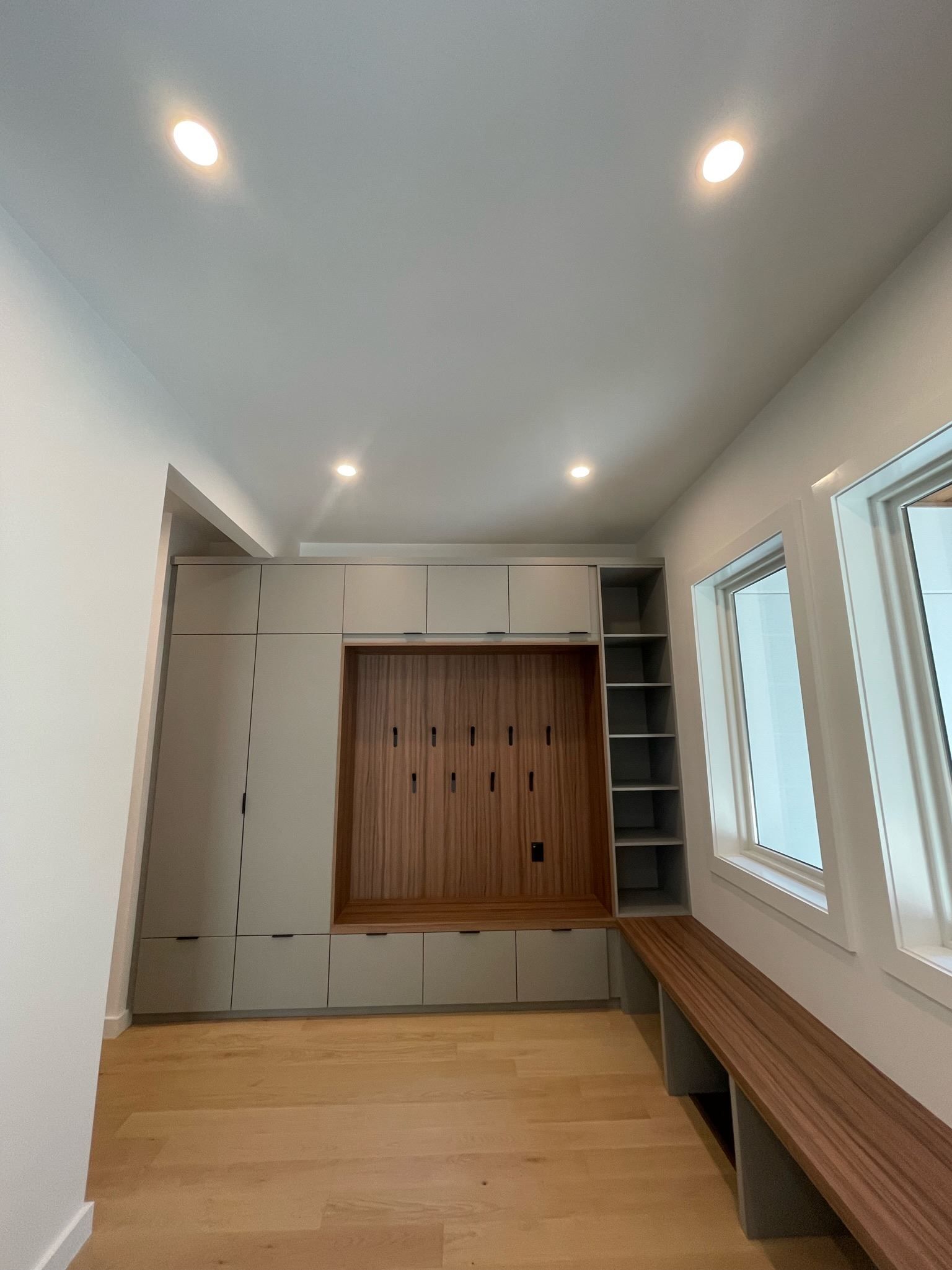 Modern narrow room with wood floor, white walls, recessed lights, built-in bench, and windowed alcove.