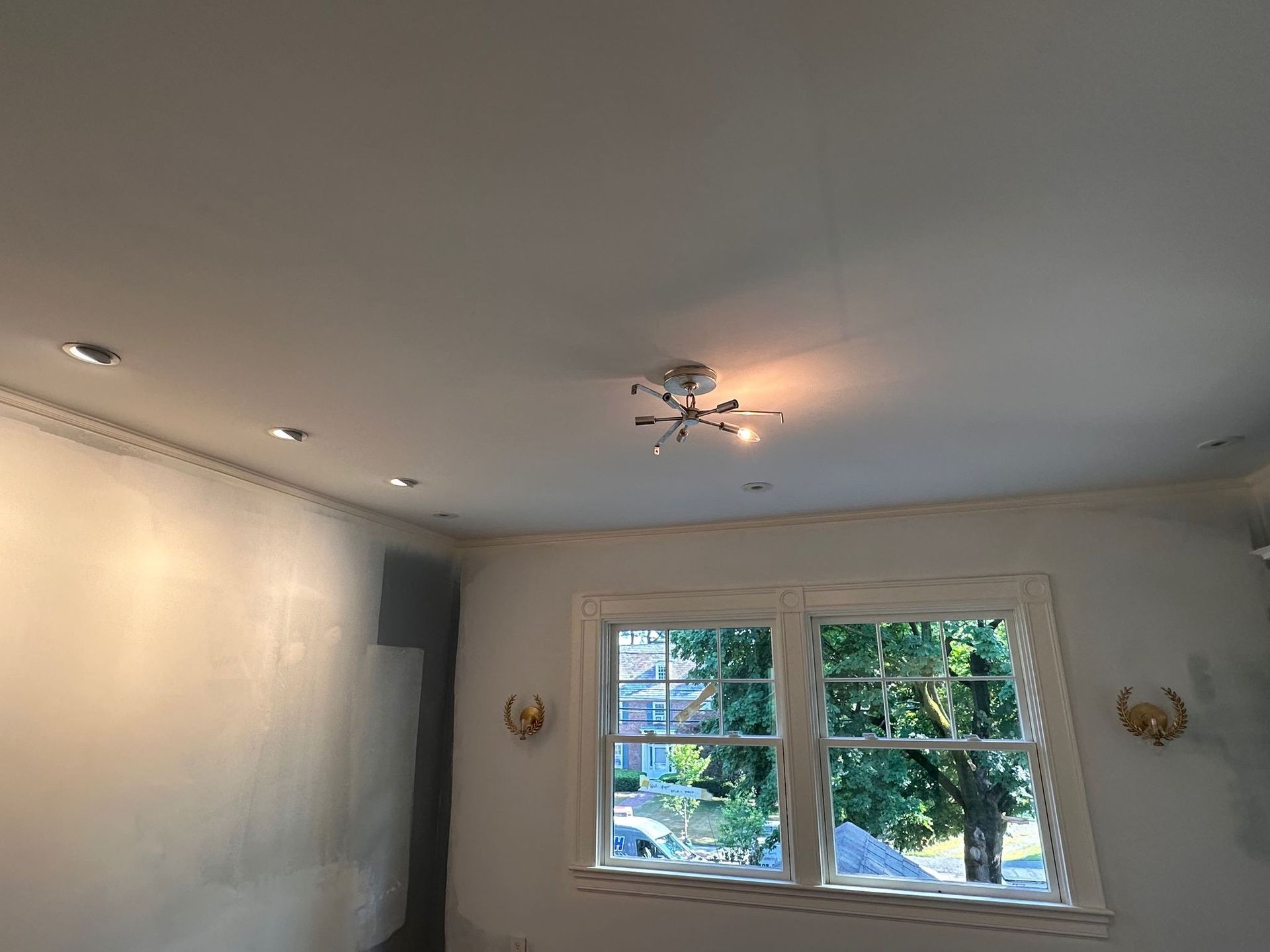 Empty white living room with ceiling lights and a window showing trees outside
