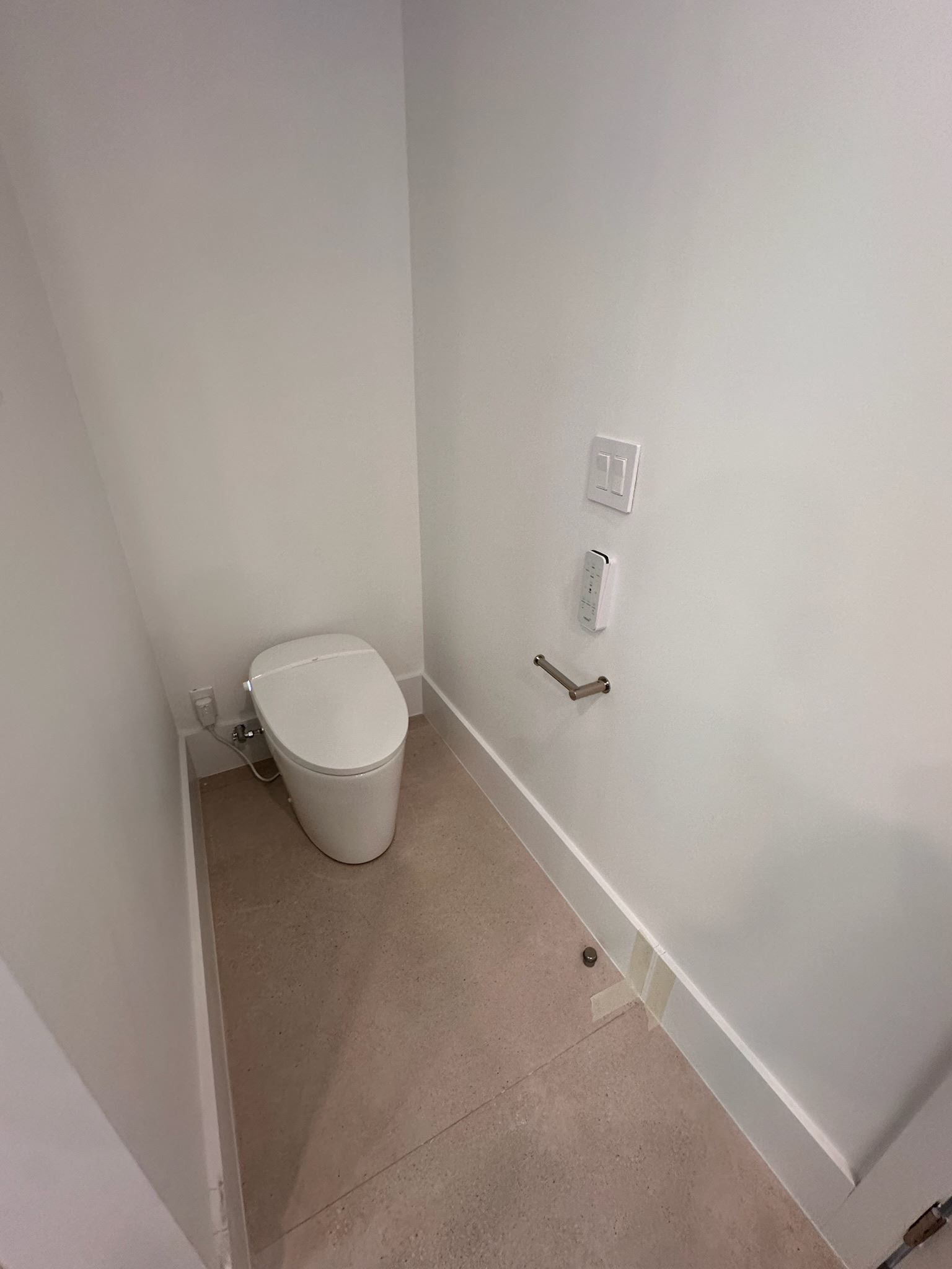 Small unfinished bathroom with a toilet and wall-mounted plumbing, beige floor, and white walls.