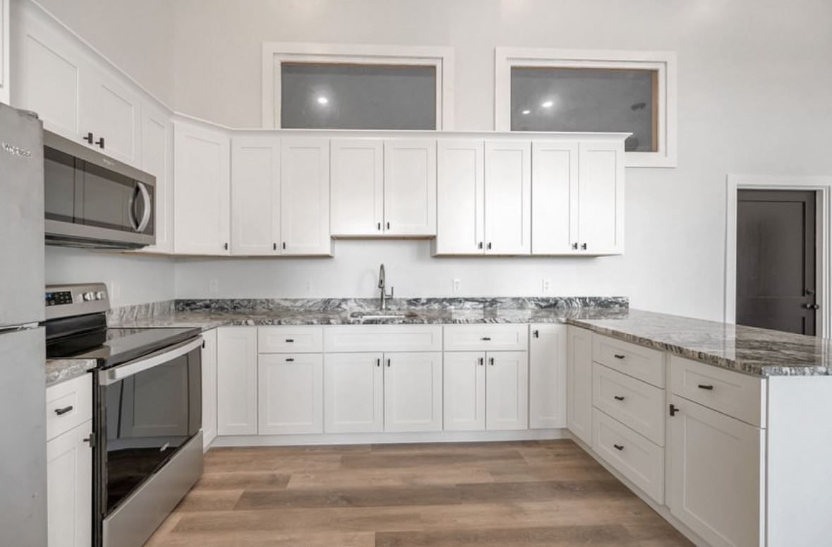 Bright modern white kitchen with granite countertops, stainless steel appliances, and wood flooring