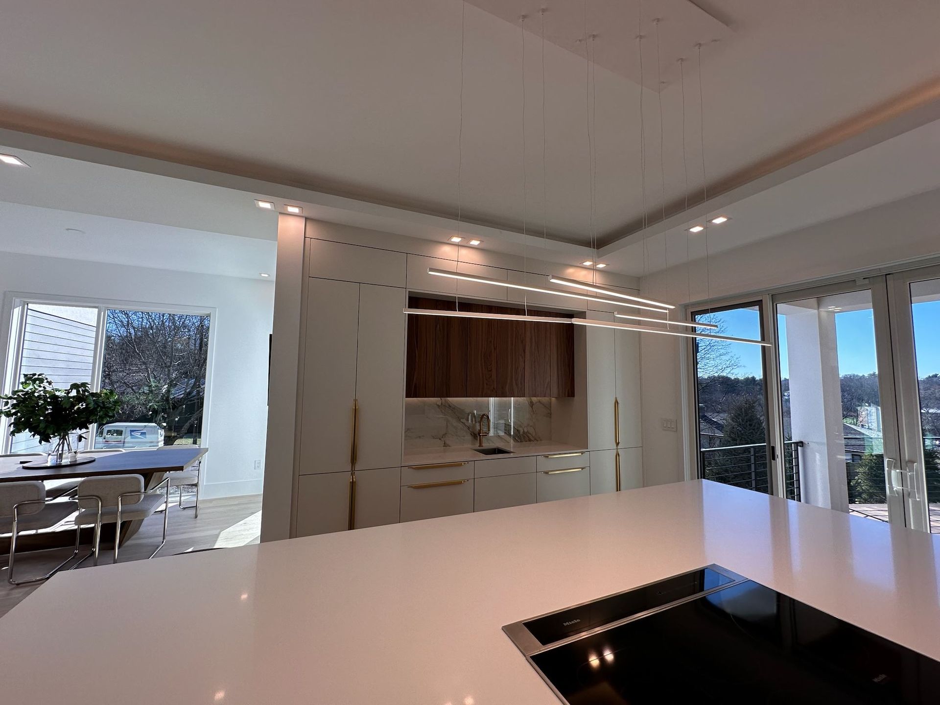 Bright modern kitchen with white island, wood cabinets, and large glass doors opening to a patio.
