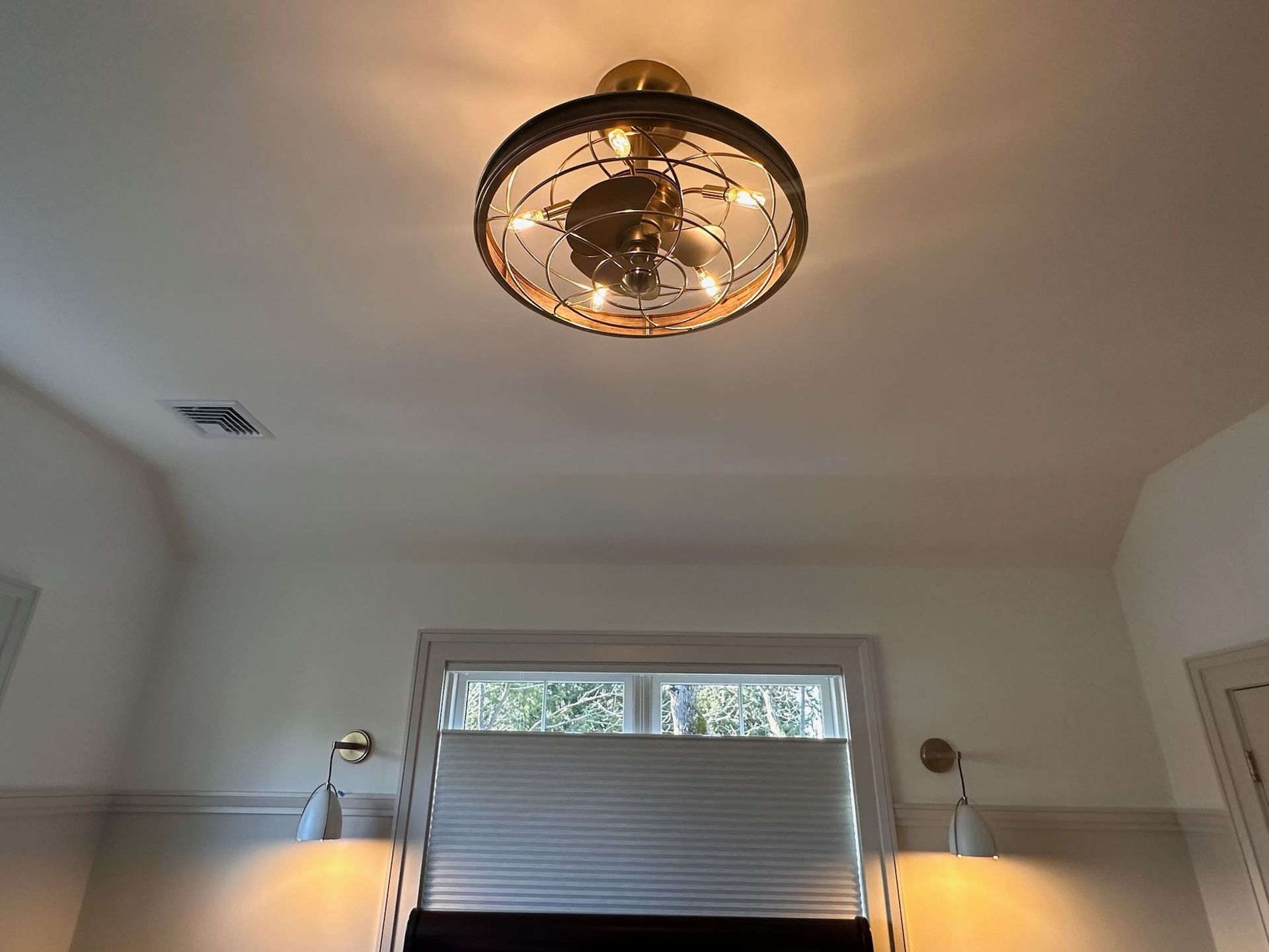 Bright ceiling light in a white room above a window with blinds and wall sconces