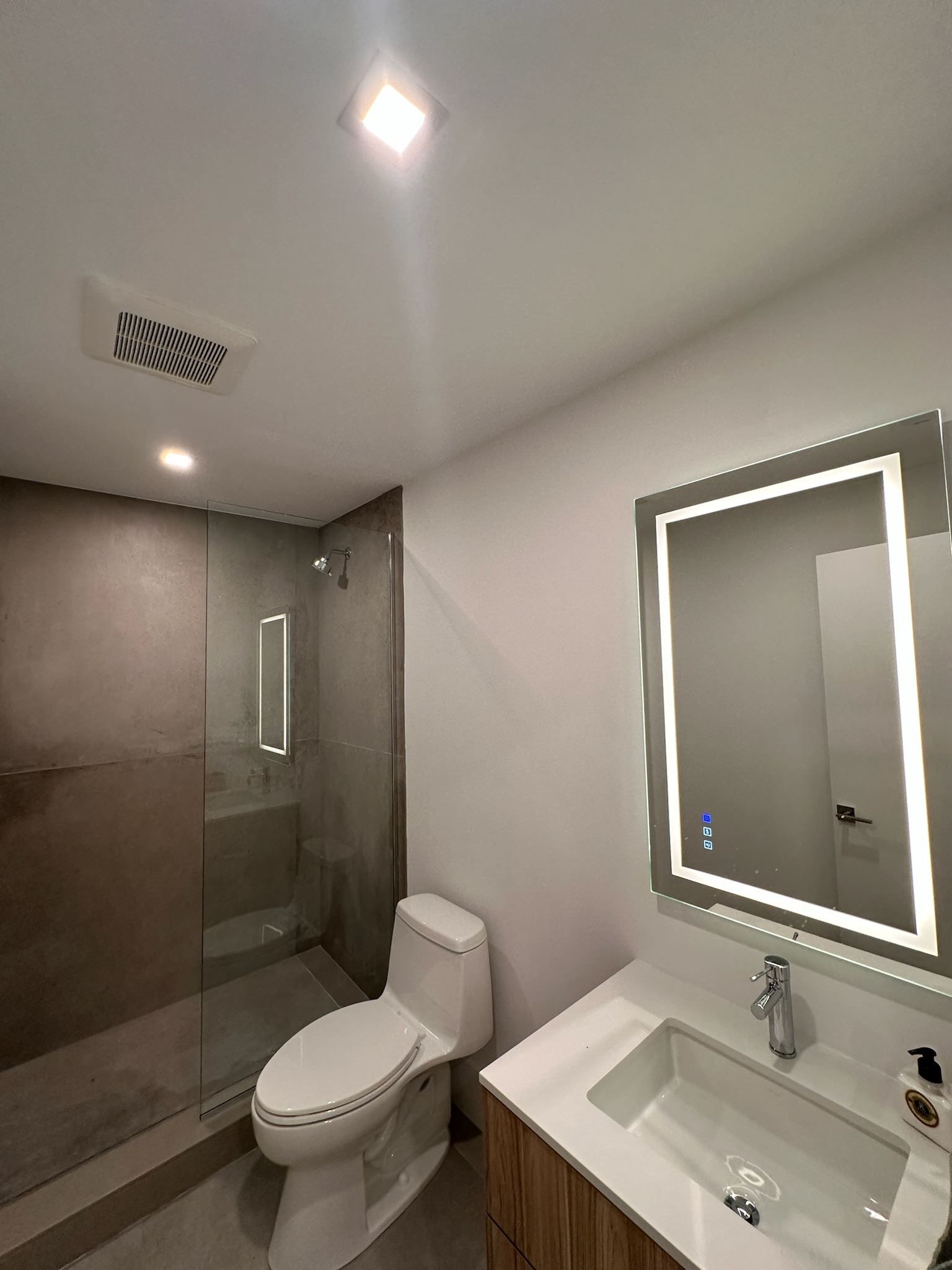 Modern bathroom with glass shower, toilet, sink, and illuminated mirror.