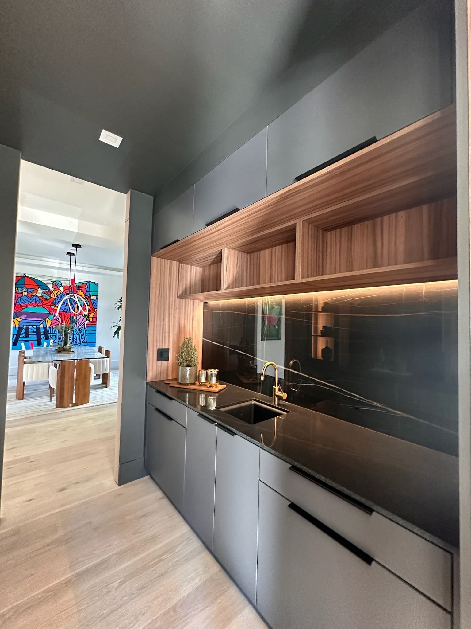 Modern kitchen with wood cabinetry, black backsplash, and stainless appliances in a sleek hallway layout