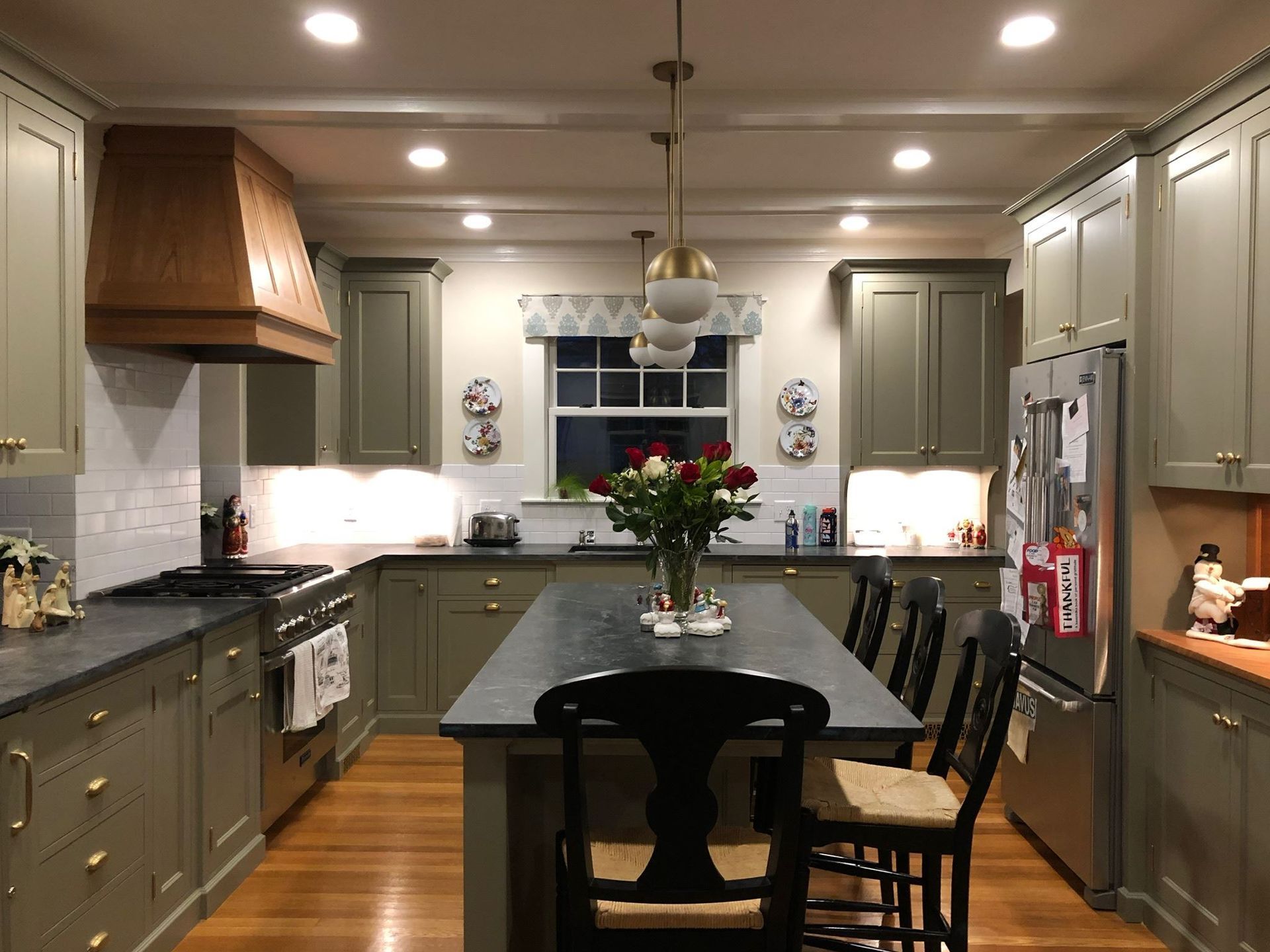 Modern kitchen with gray cabinets, black island, and pendant lights beneath a central window.