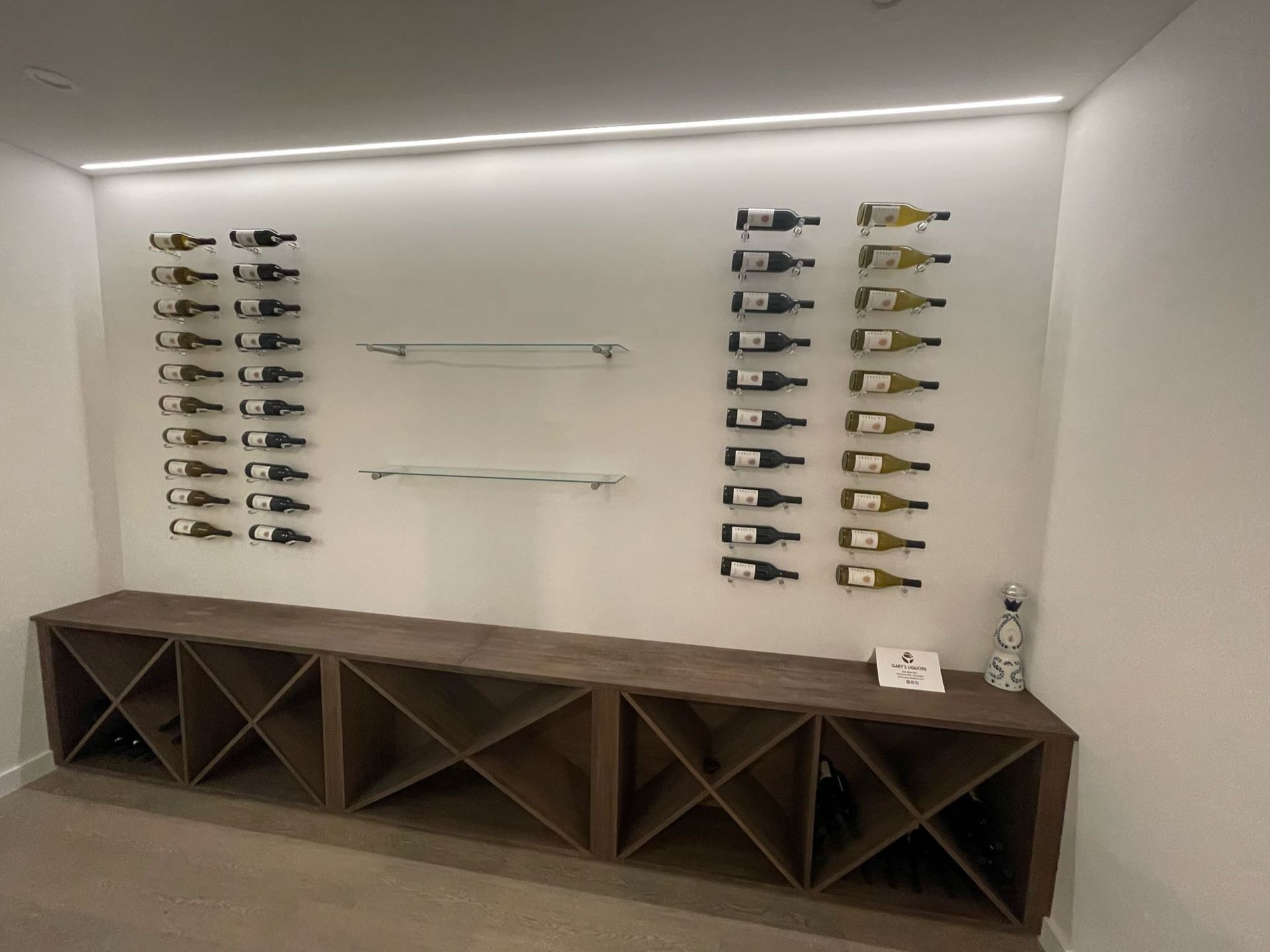 Wall-mounted wine display above a dark wood wine rack in a modern room