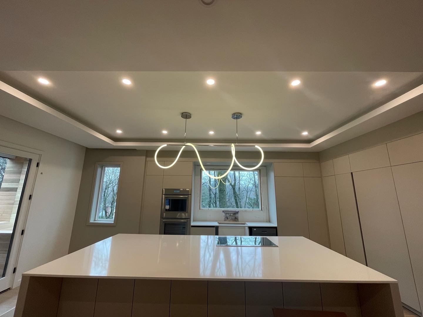 Modern kitchen with white island, built-in cabinets, recessed lights, and a contemporary pendant fixture.