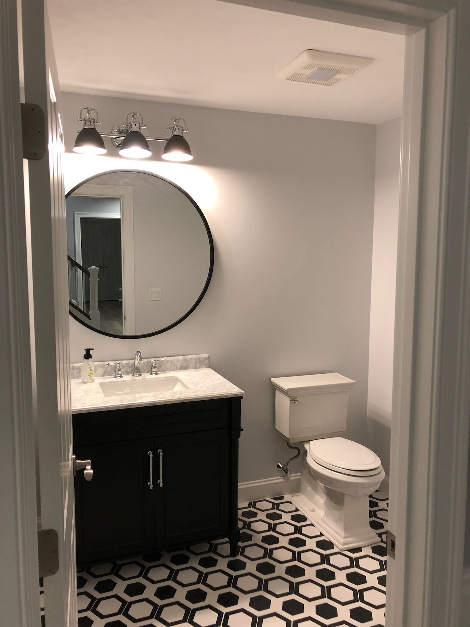 Small bathroom with black vanity, round mirror, white toilet, and black-and-white patterned floor tiles