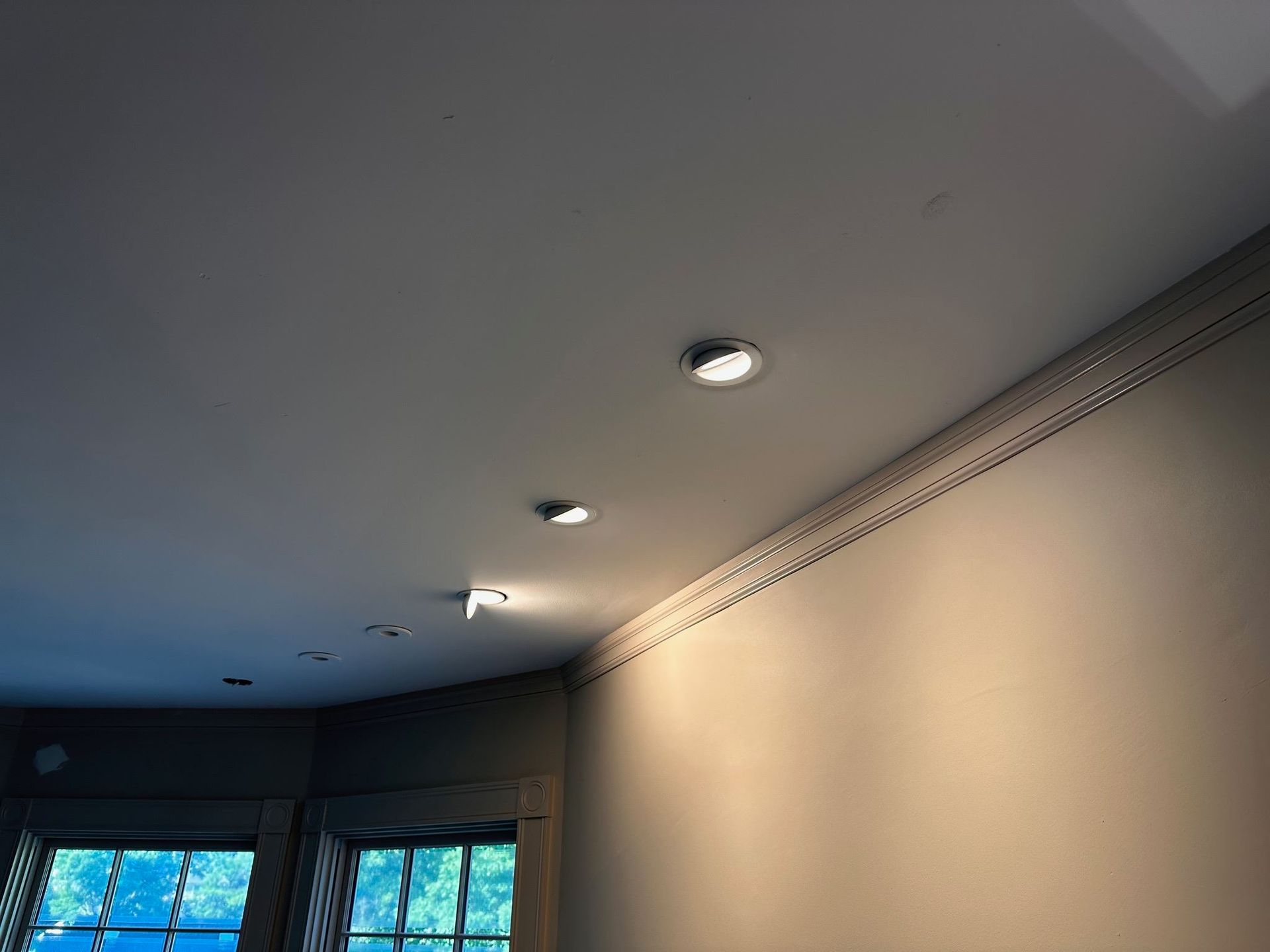 Ceiling with recessed lights and a wall-mounted track, above a room with windows.