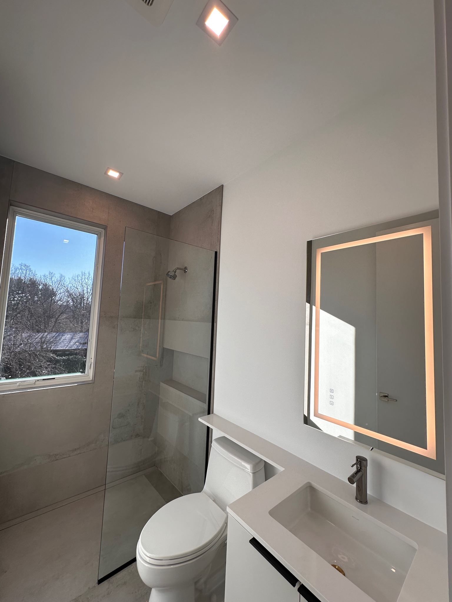 Modern bathroom with walk-in shower, wall-mounted toilet, and lit vanity mirror
