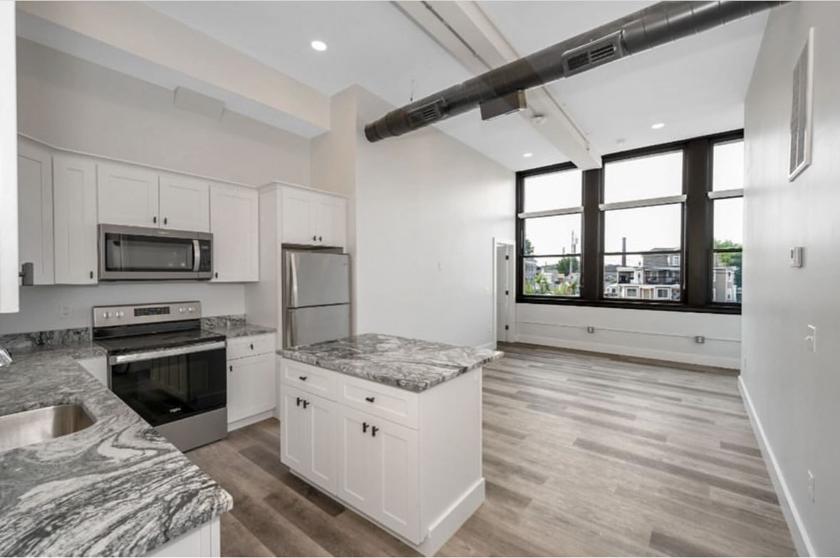 Bright modern kitchen with white cabinets, marble island, and large windows in an open loft living space