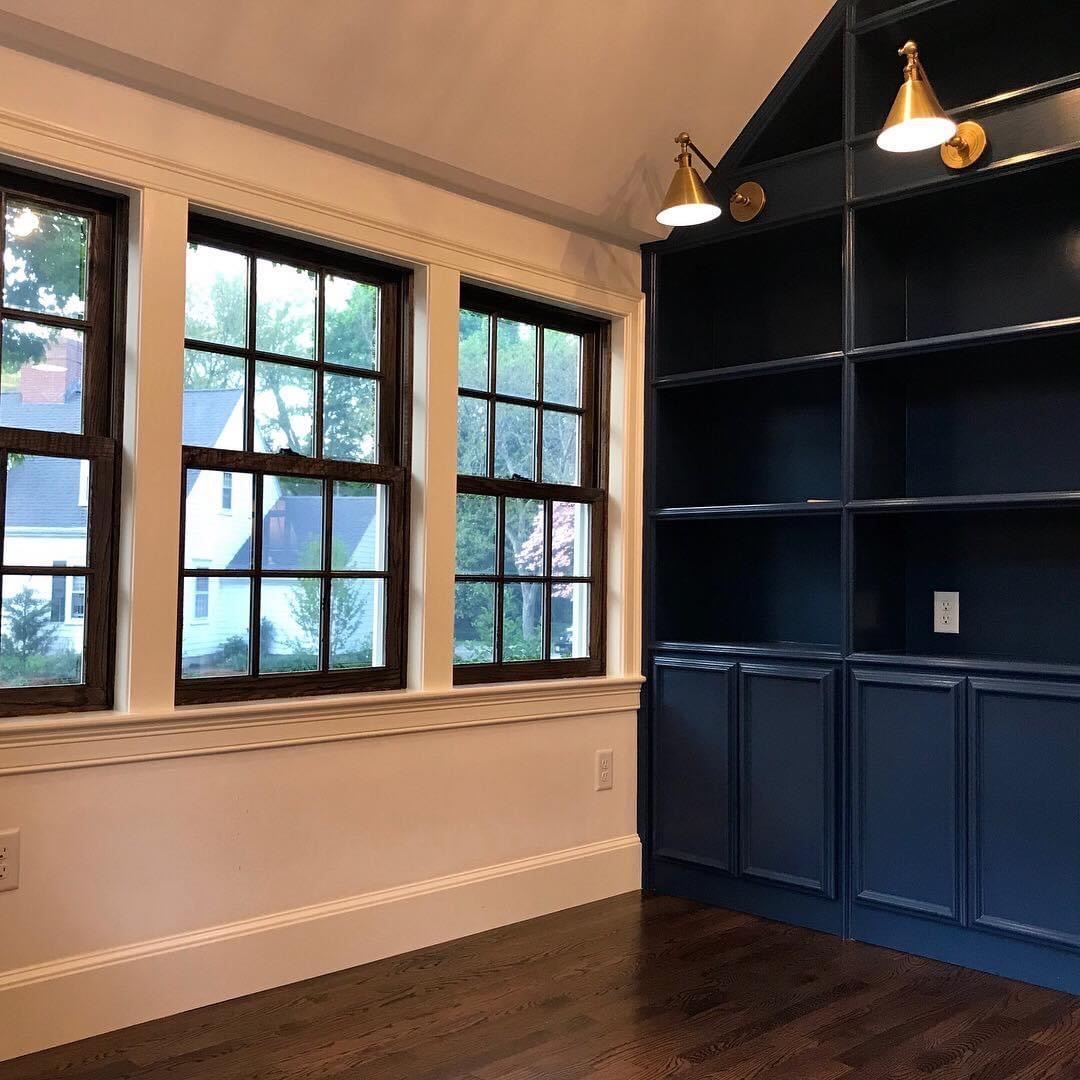 Empty room with dark built-in shelves, pendant lights, wood floors, and windows along one wall
