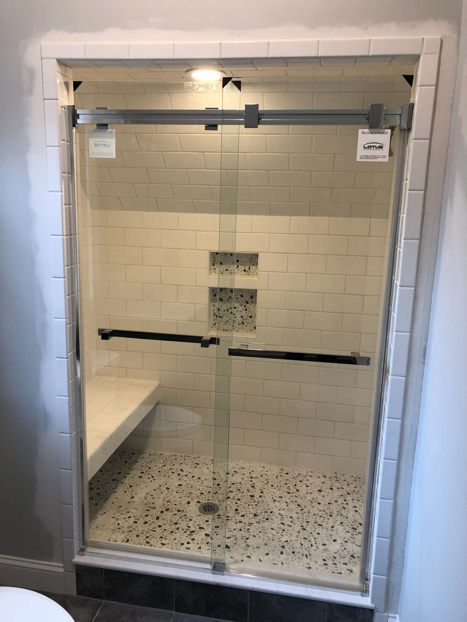Glass shower stall with white tile walls and a black-speckled shower floor in a bathroom