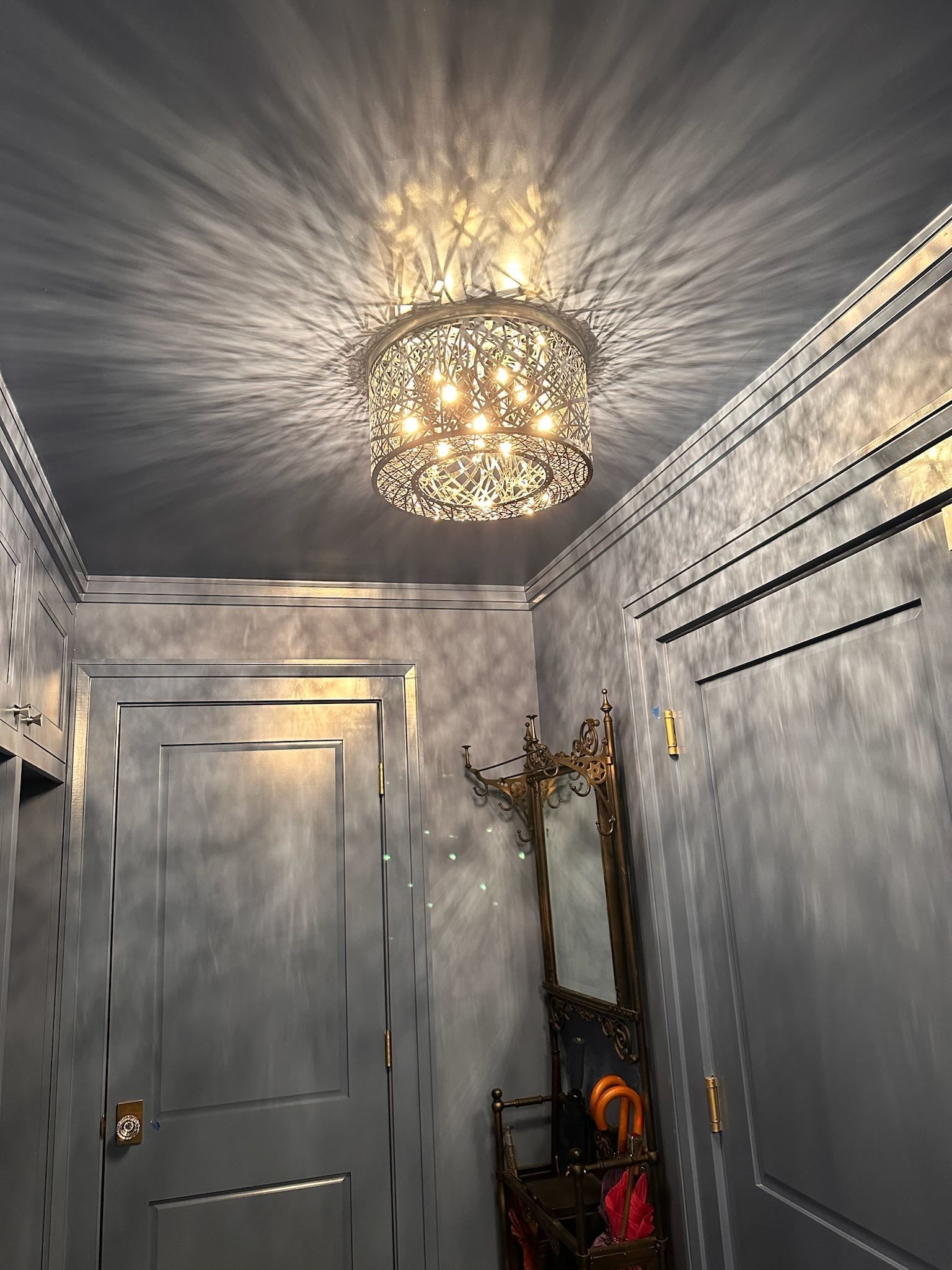 Gray hallway with ornate ceiling light, paneled doors, and a decorative mirror at the end.