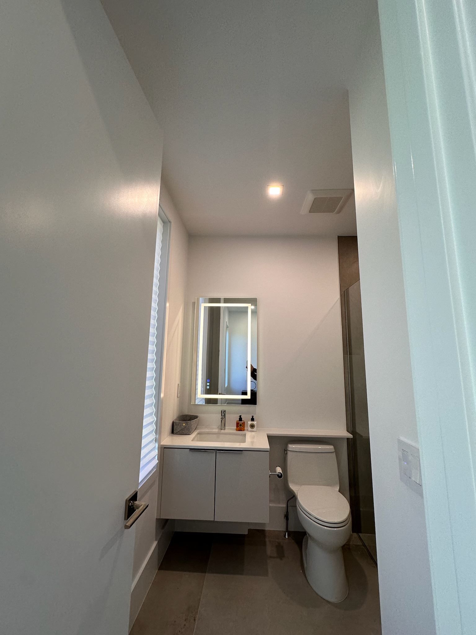 Narrow white bathroom with vanity, mirror, toilet, window, and ceiling light