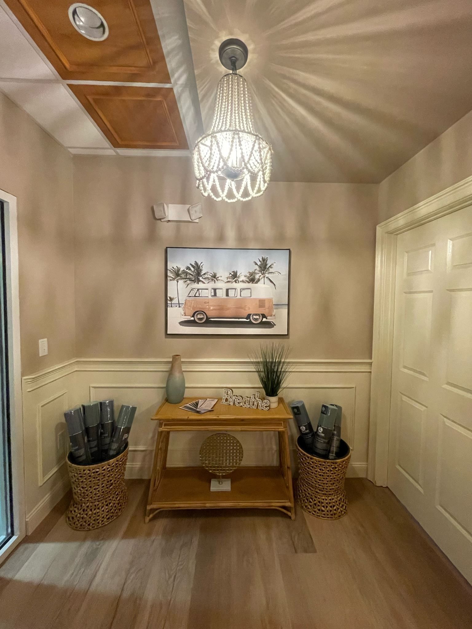 Small beige hallway with a wood console table, wall art, ceiling light, and wicker umbrella stands.