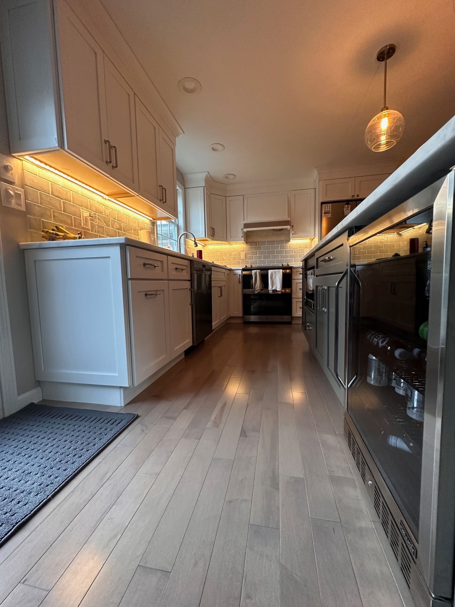 Modern kitchen with white cabinets, wooden floor, warm under-cabinet lights, and black appliances