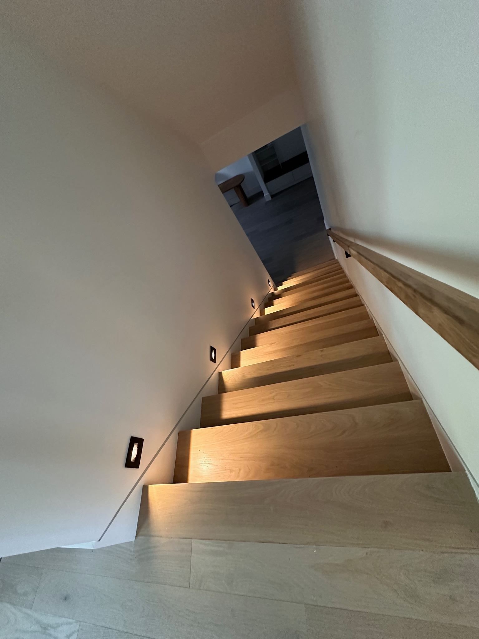 Indoor staircase with wooden steps, handrail, and wall lights, viewed upward toward a landing