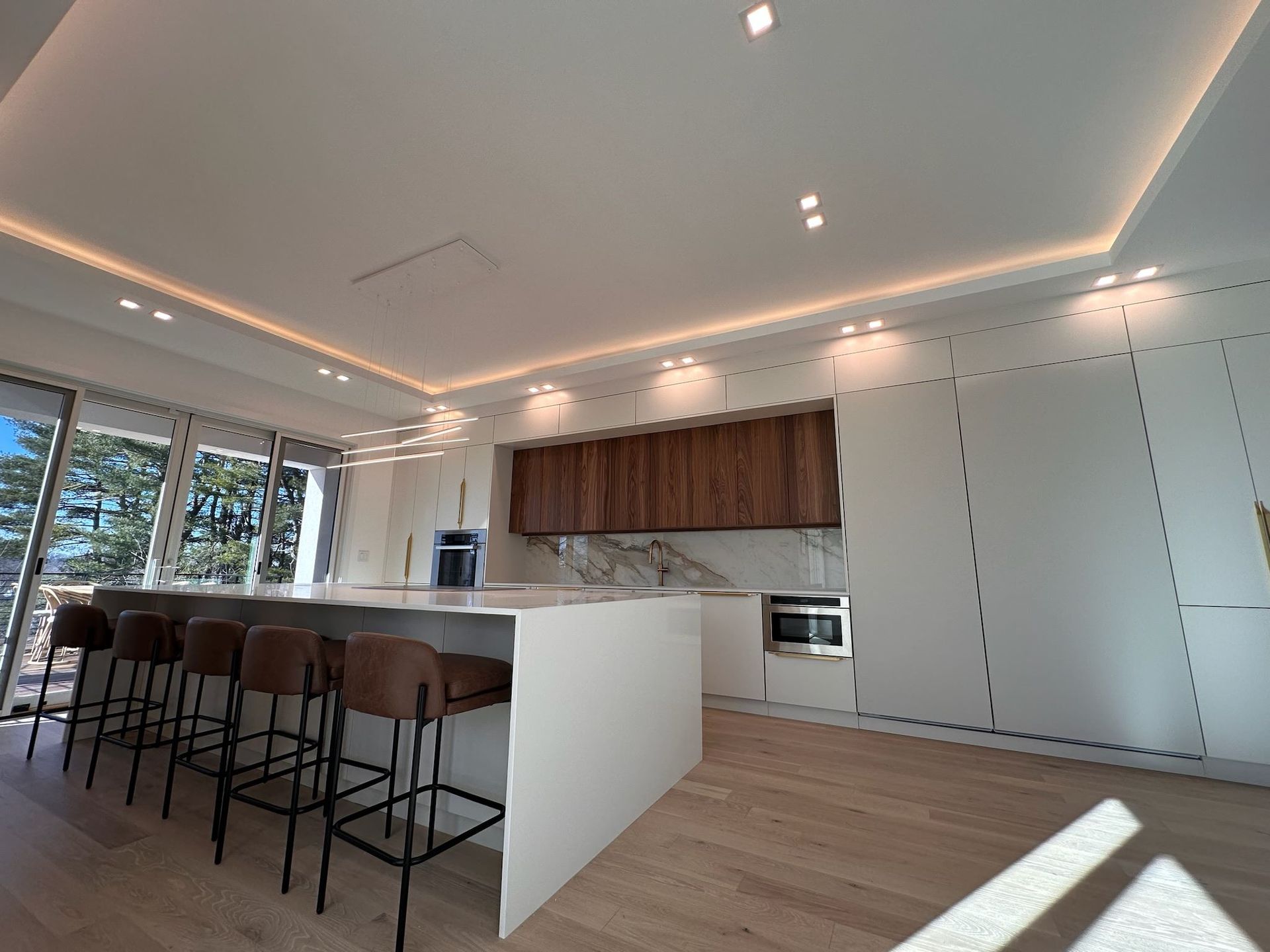 Modern open-plan kitchen with white island, wood cabinets, bar stools, and recessed ceiling lights