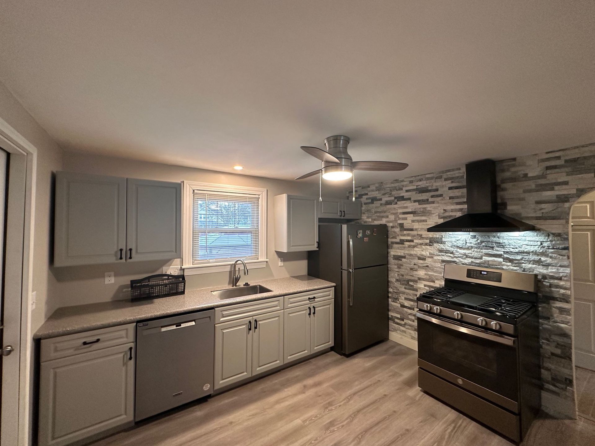 Modern kitchen with gray cabinets, stainless appliances, stone backsplash, and a ceiling fan