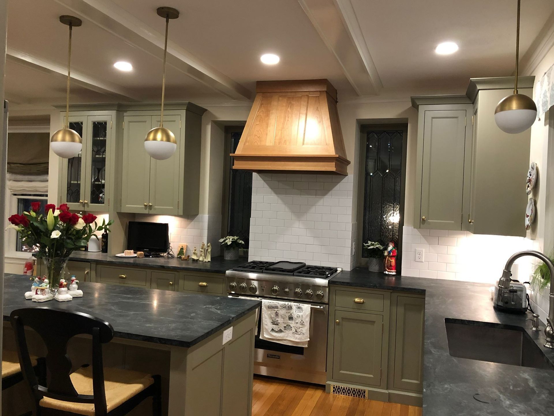 Modern kitchen with dark island, white cabinets, copper range hood, and pendant lights