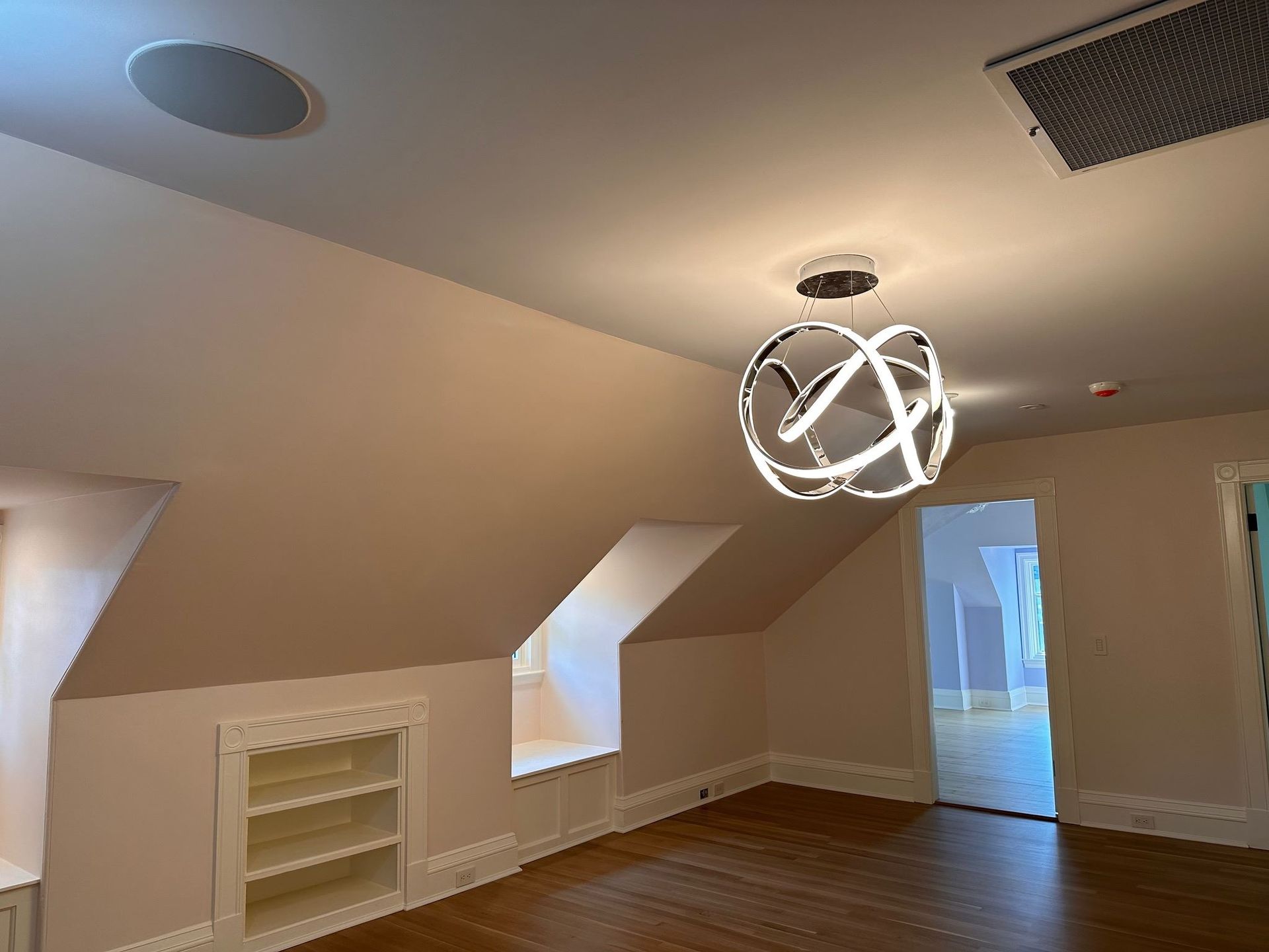 Empty beige room with sloped ceiling, skylights, wood floor, and modern pendant light
