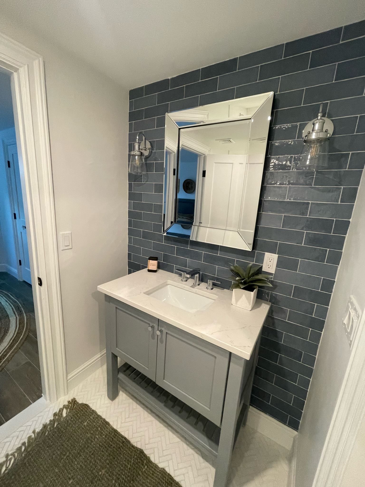 Small bathroom vanity with white sink, mirror, blue shiplap accent wall, and gray cabinet.