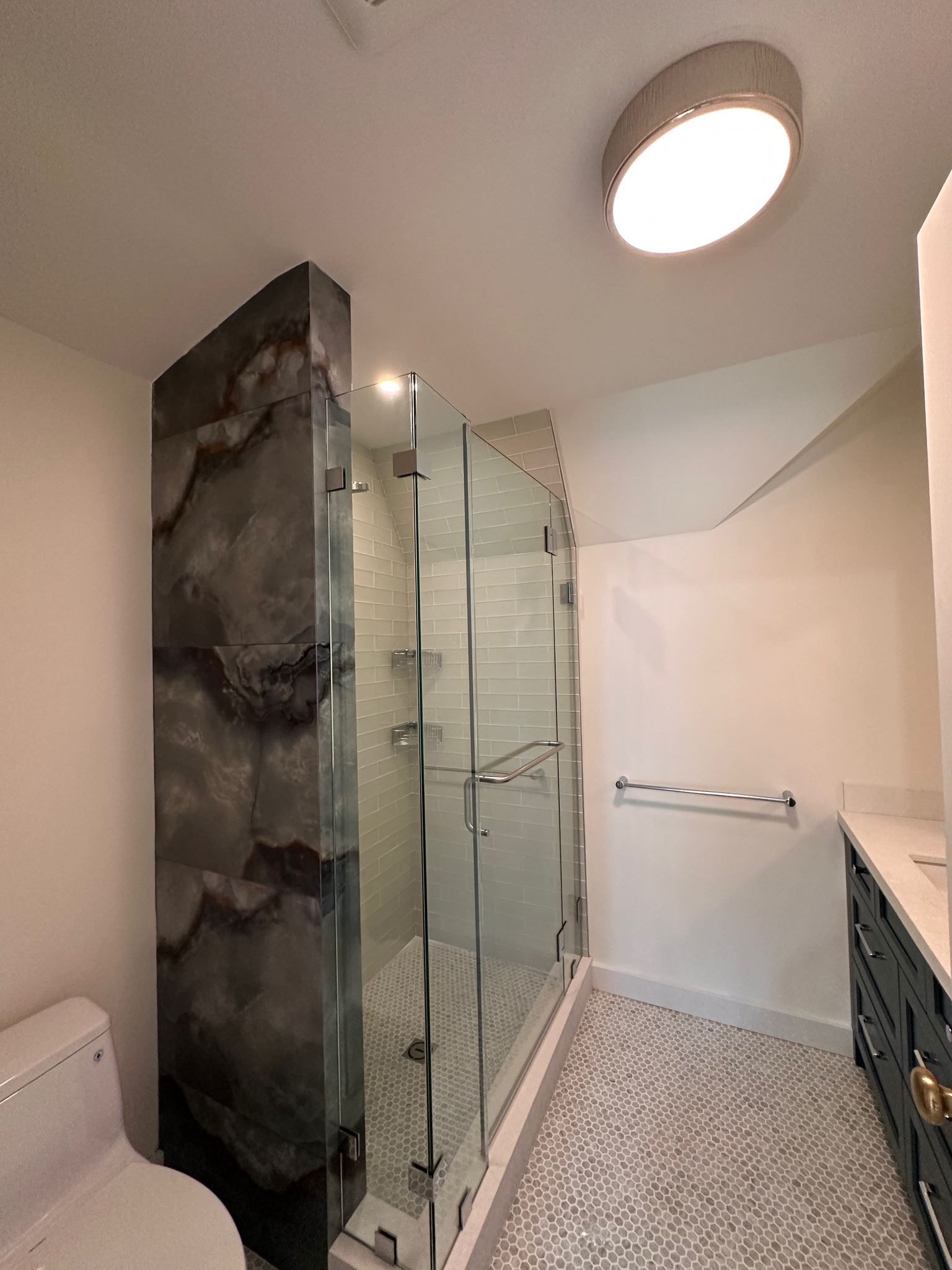 Modern bathroom with glass shower, pebble floor, stone accent wall, and round ceiling light