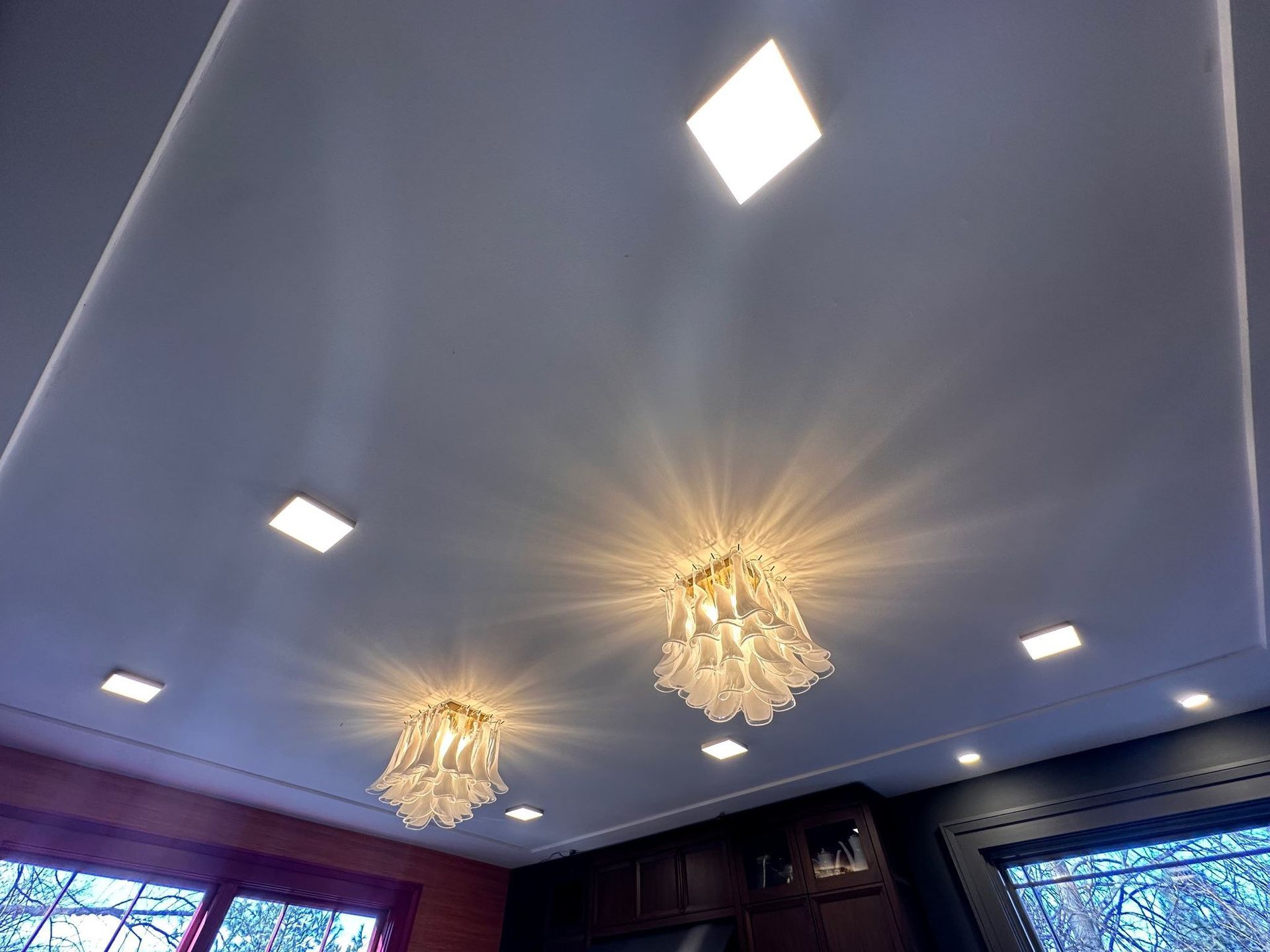 Ceiling with recessed lights and two chandeliers in a dim room