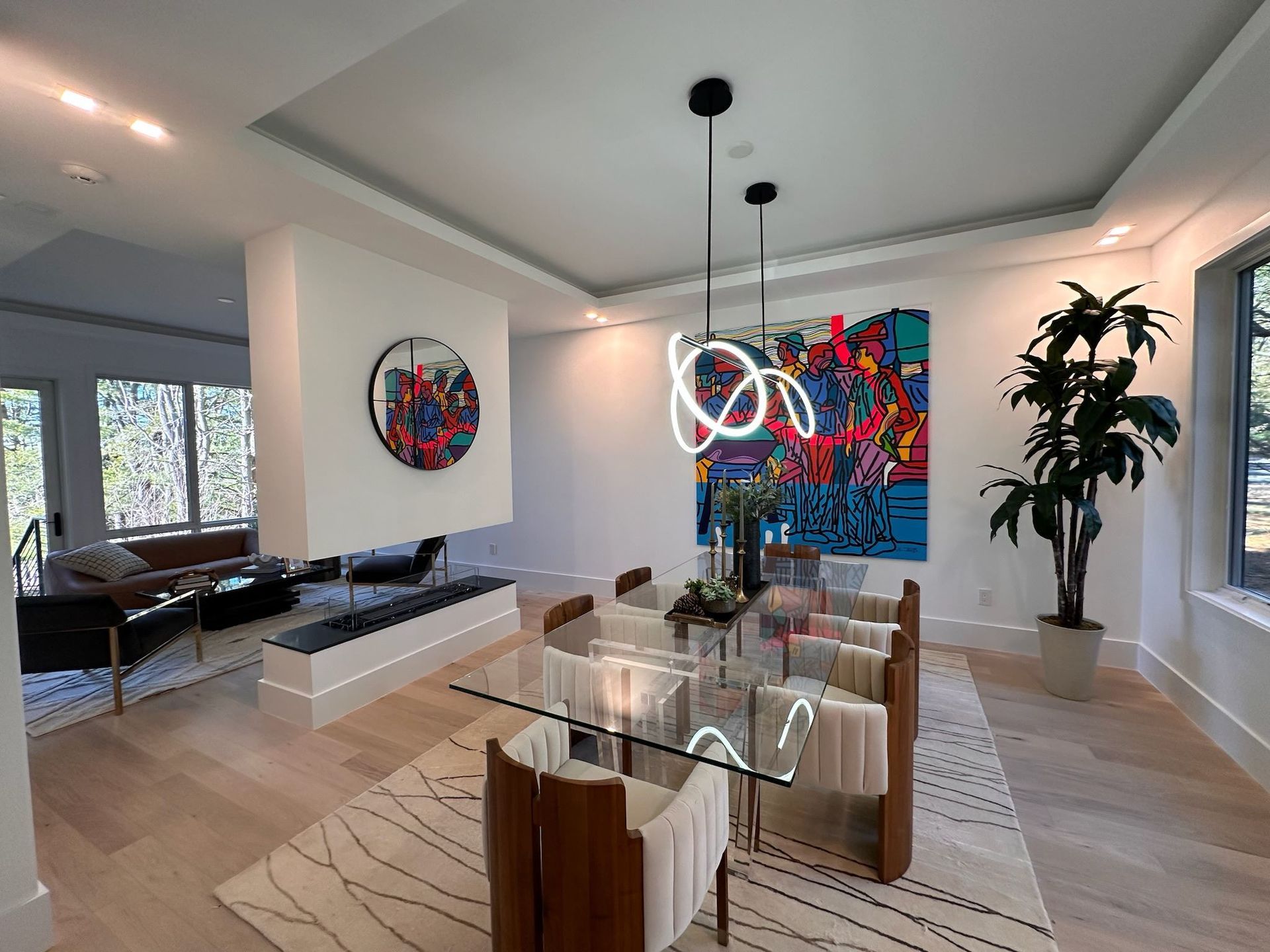 Modern dining room with glass table, hanging pendant lights, colorful wall art, and potted plant