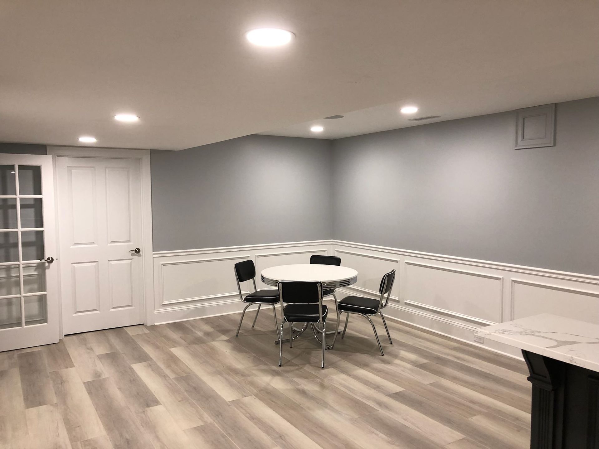 Empty dining room with gray walls, wood floors, white trim, and a round table with chairs under recessed lights