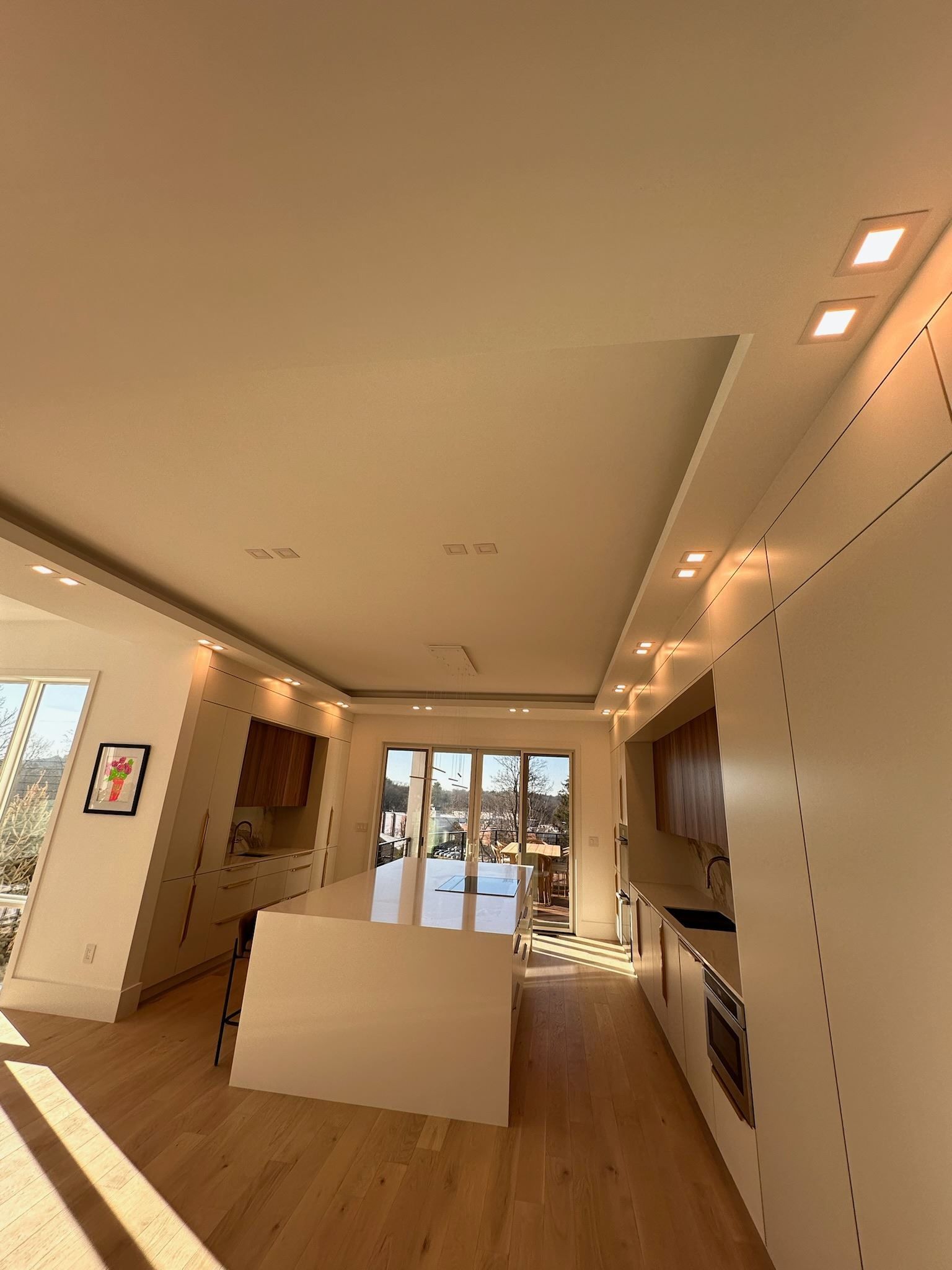 Modern living room with wood floors, white walls, recessed lighting, and a central white partition.
