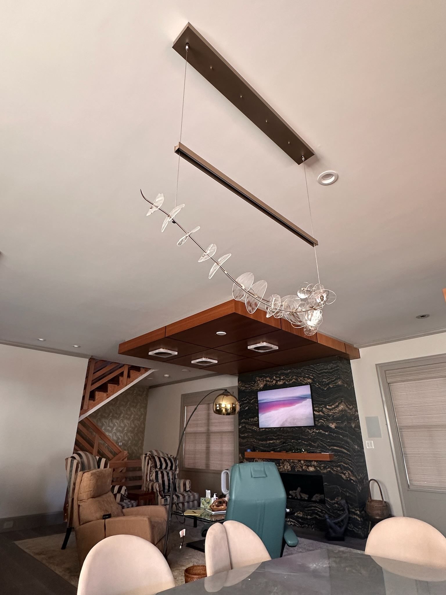 Modern living room with chandelier, wood ceiling accents, TV, fireplace, and white dining chairs
