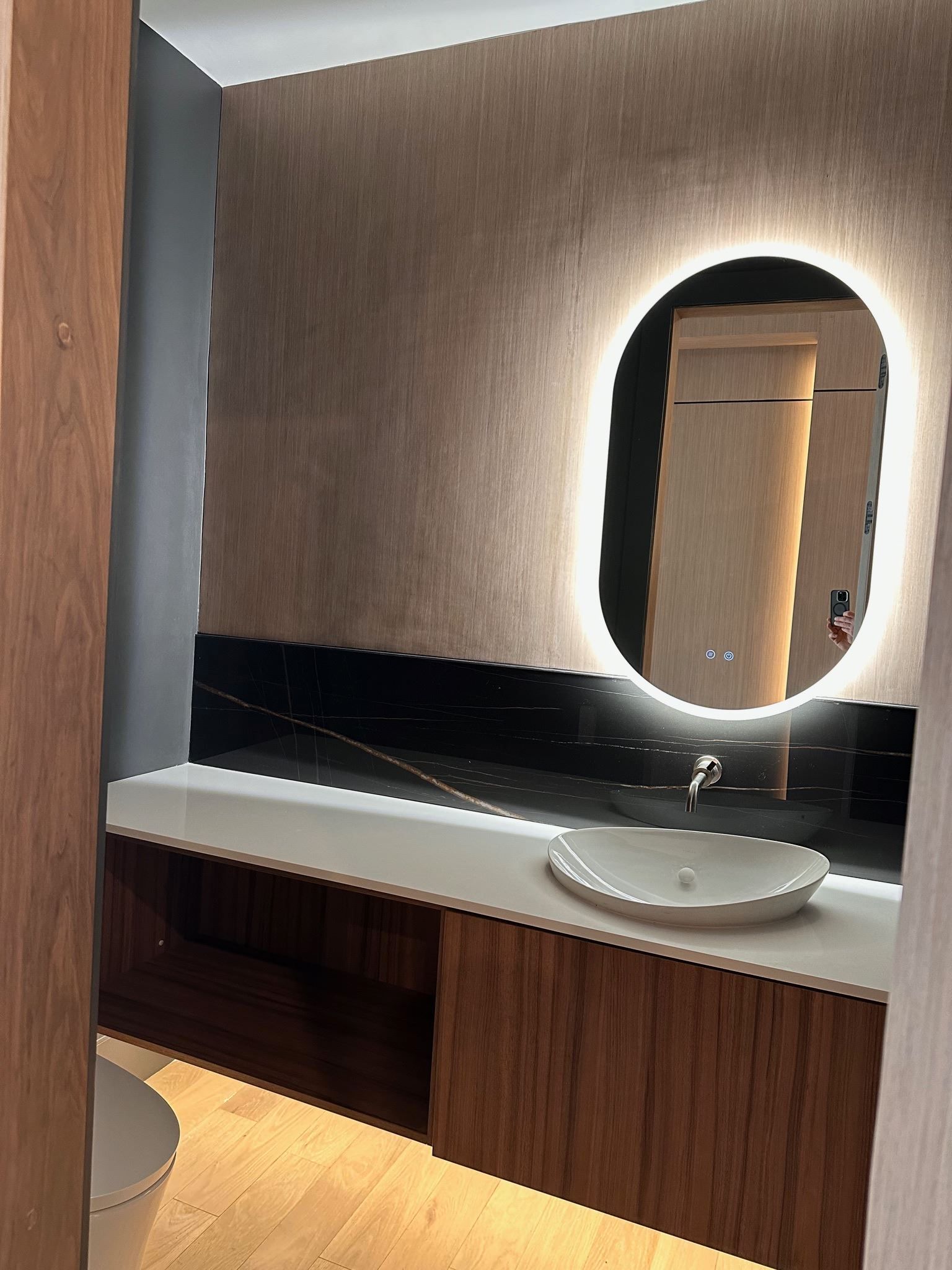 Modern bathroom vanity with wood cabinets, white countertop, oval mirror, and sink under warm lighting