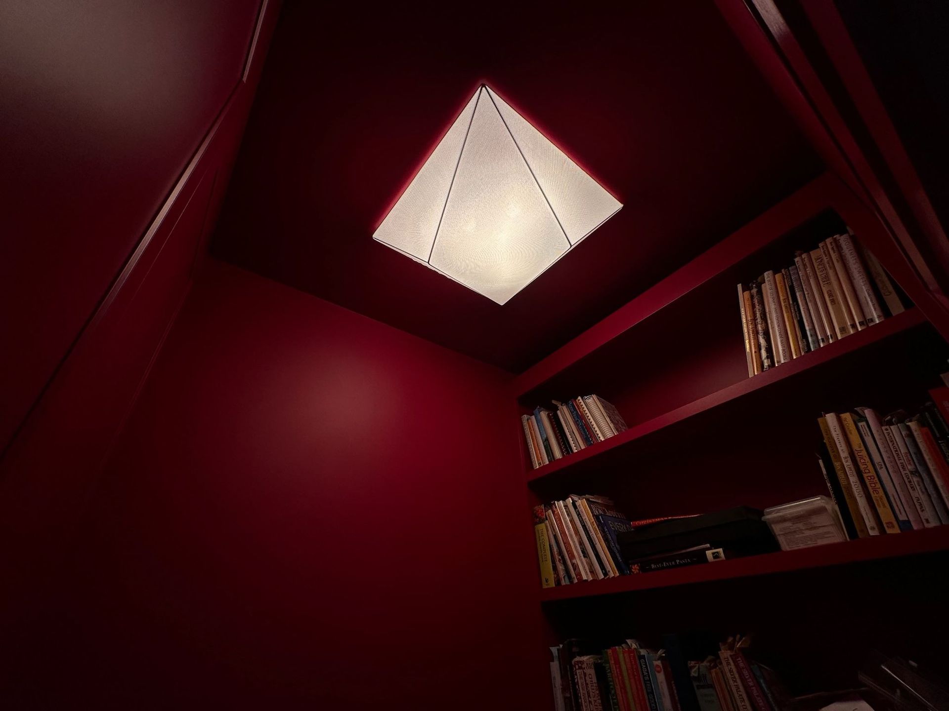 Red walls and bookshelves beneath a glowing white ceiling light in a cozy corner nook