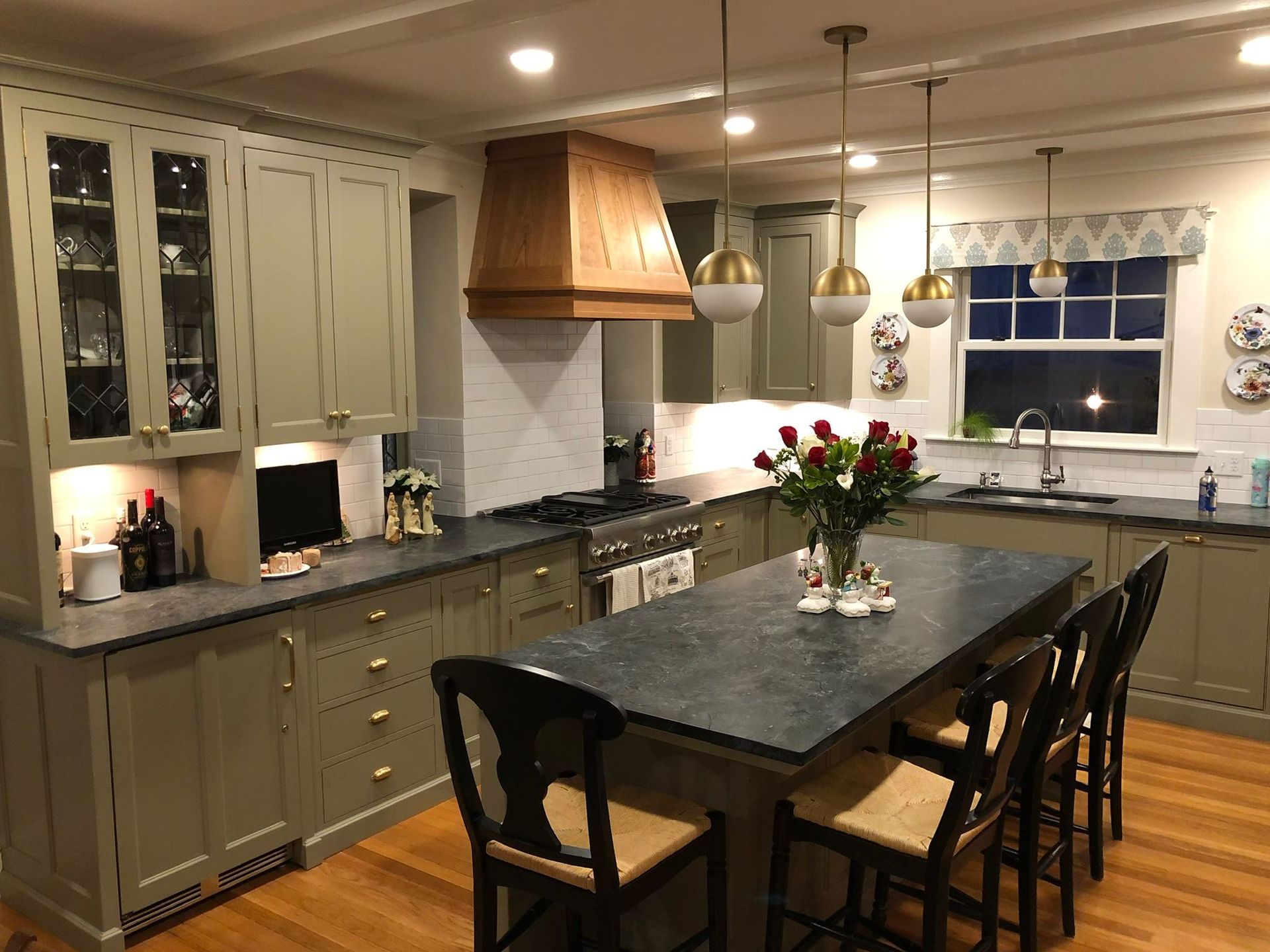 Modern kitchen with gray cabinets, granite island, pendant lights, and a vase of flowers on the table