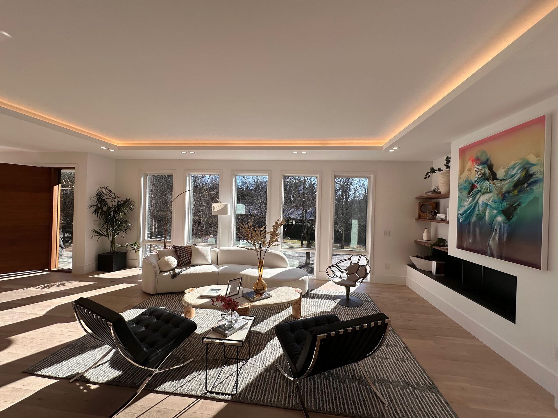 Modern living room with floor-to-ceiling windows, black chairs, beige sofa, and large colorful wall art