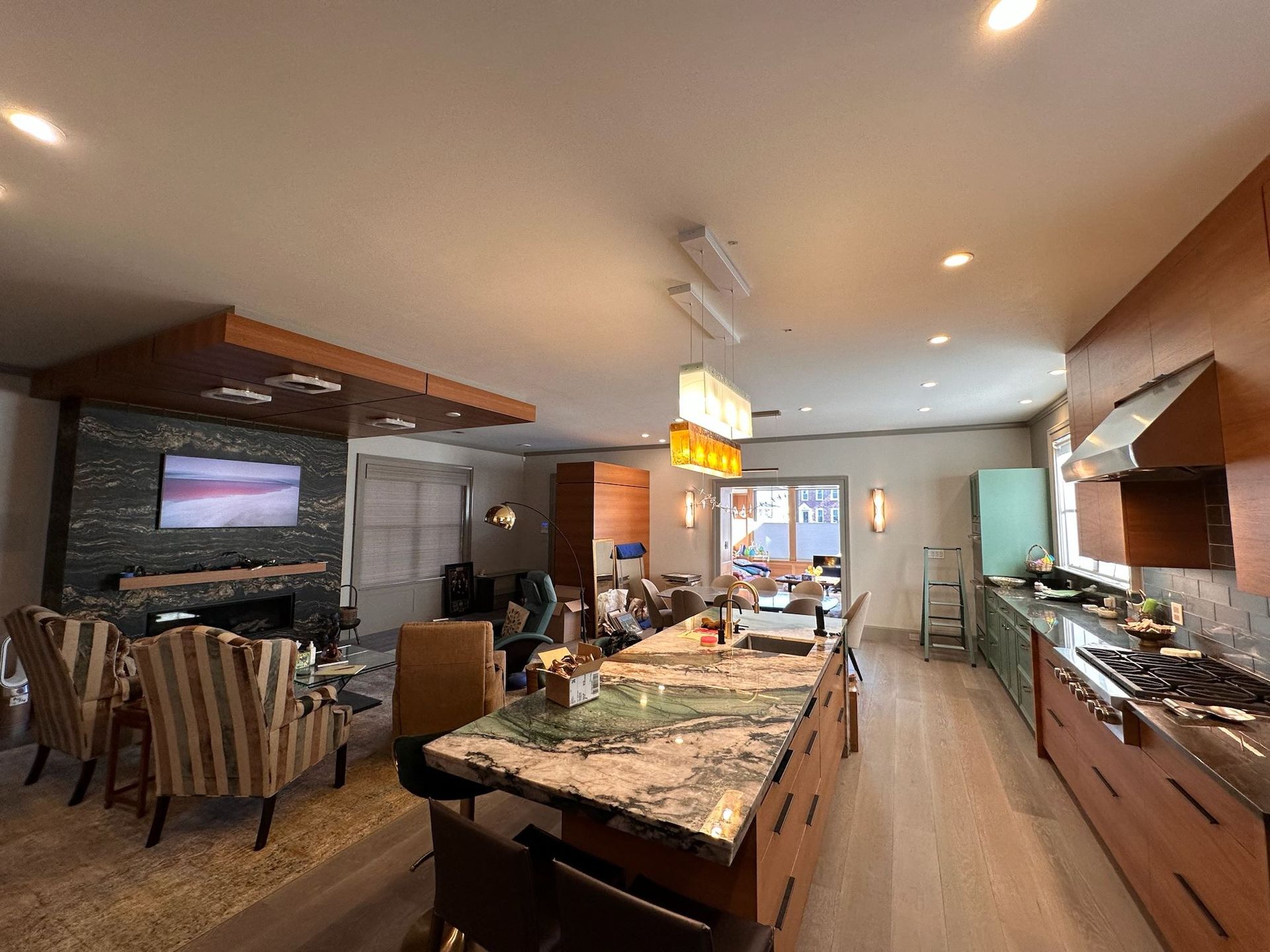 Modern kitchen and dining area with marble island, wood cabinets, stone fireplace, and recessed lighting