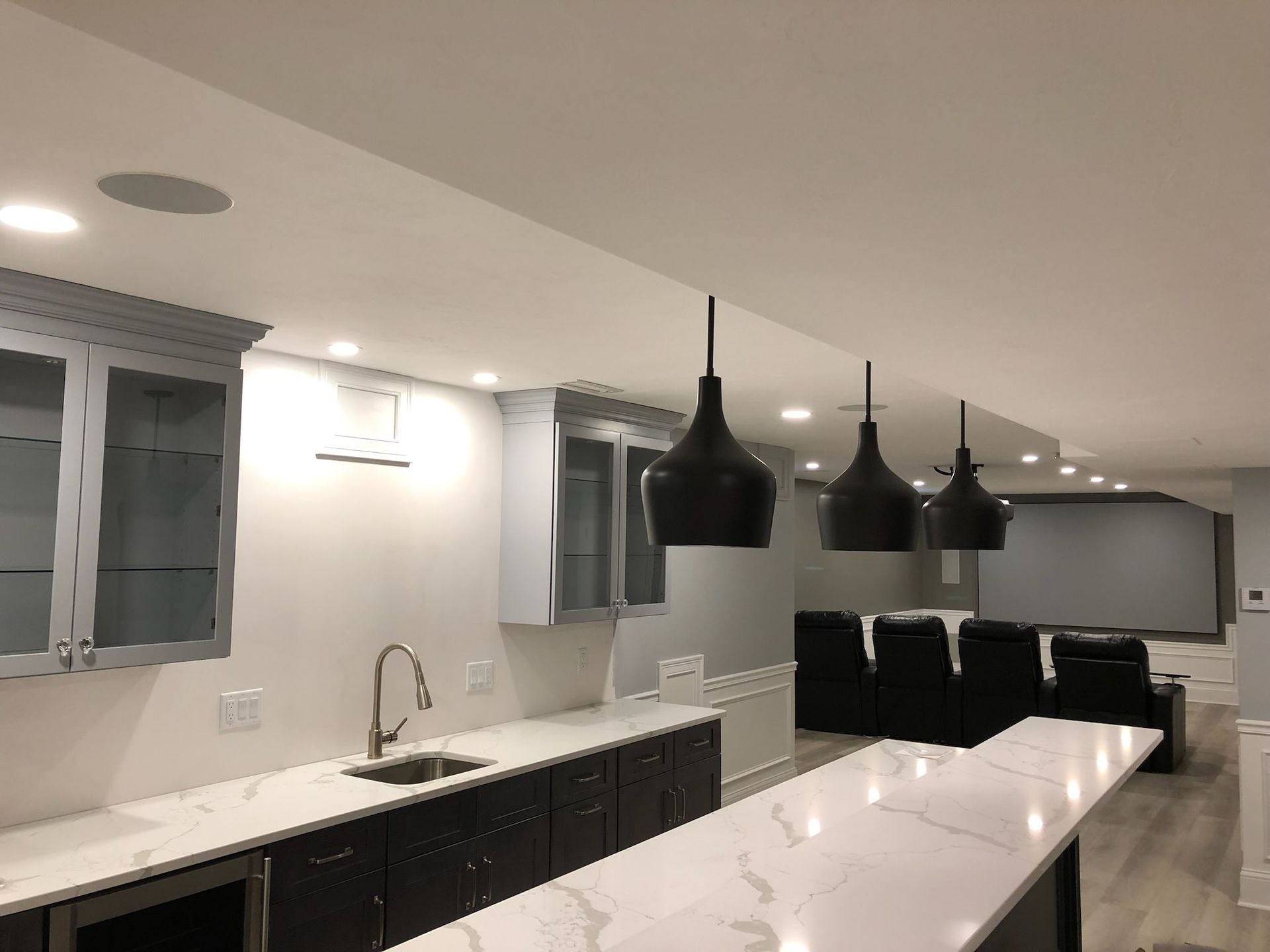 Modern kitchen with white island, black pendant lights, and dark cabinets in an open living area